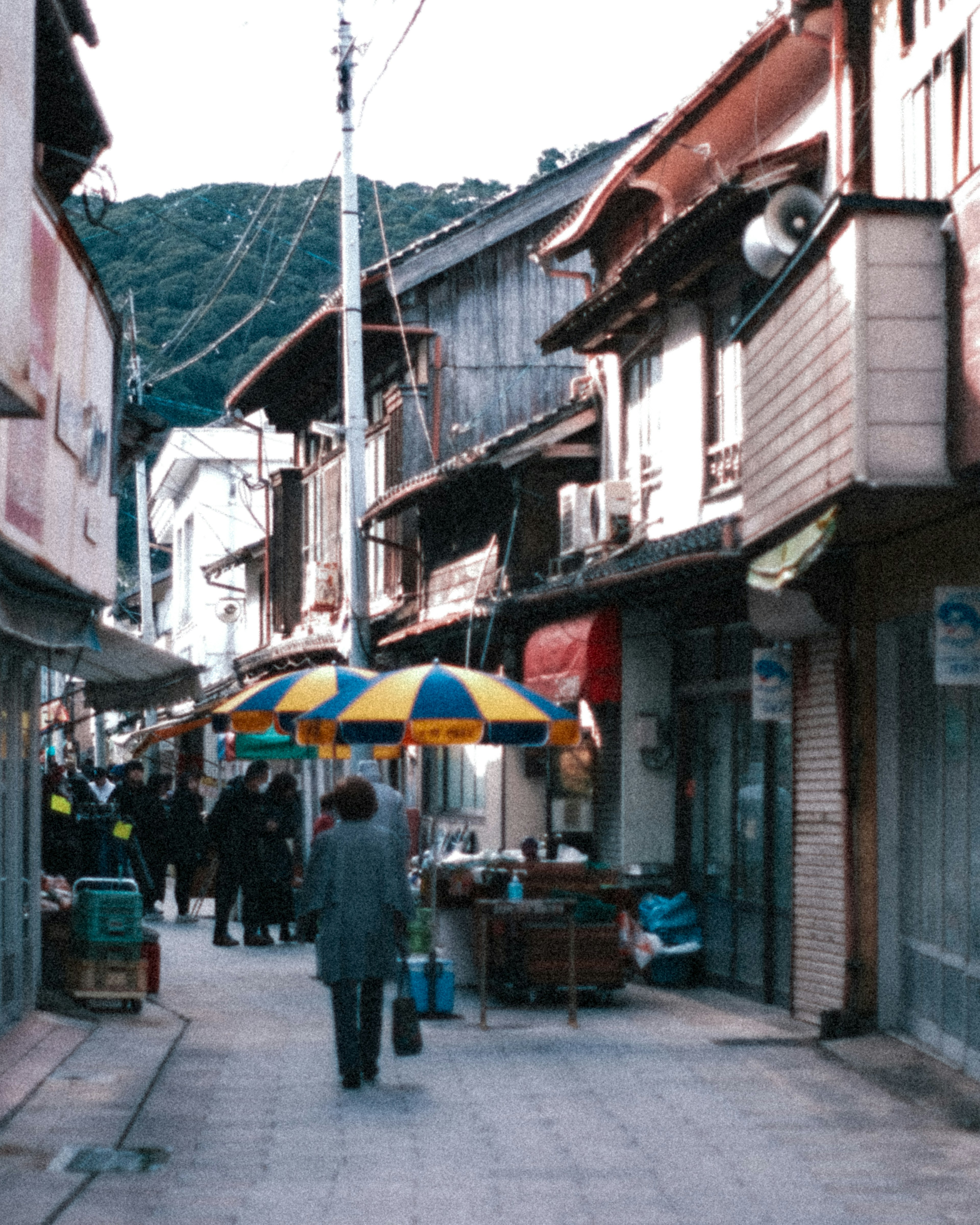 Vista pintoresca de una antigua calle comercial con montañas de fondo personas caminando bajo paraguas coloridos