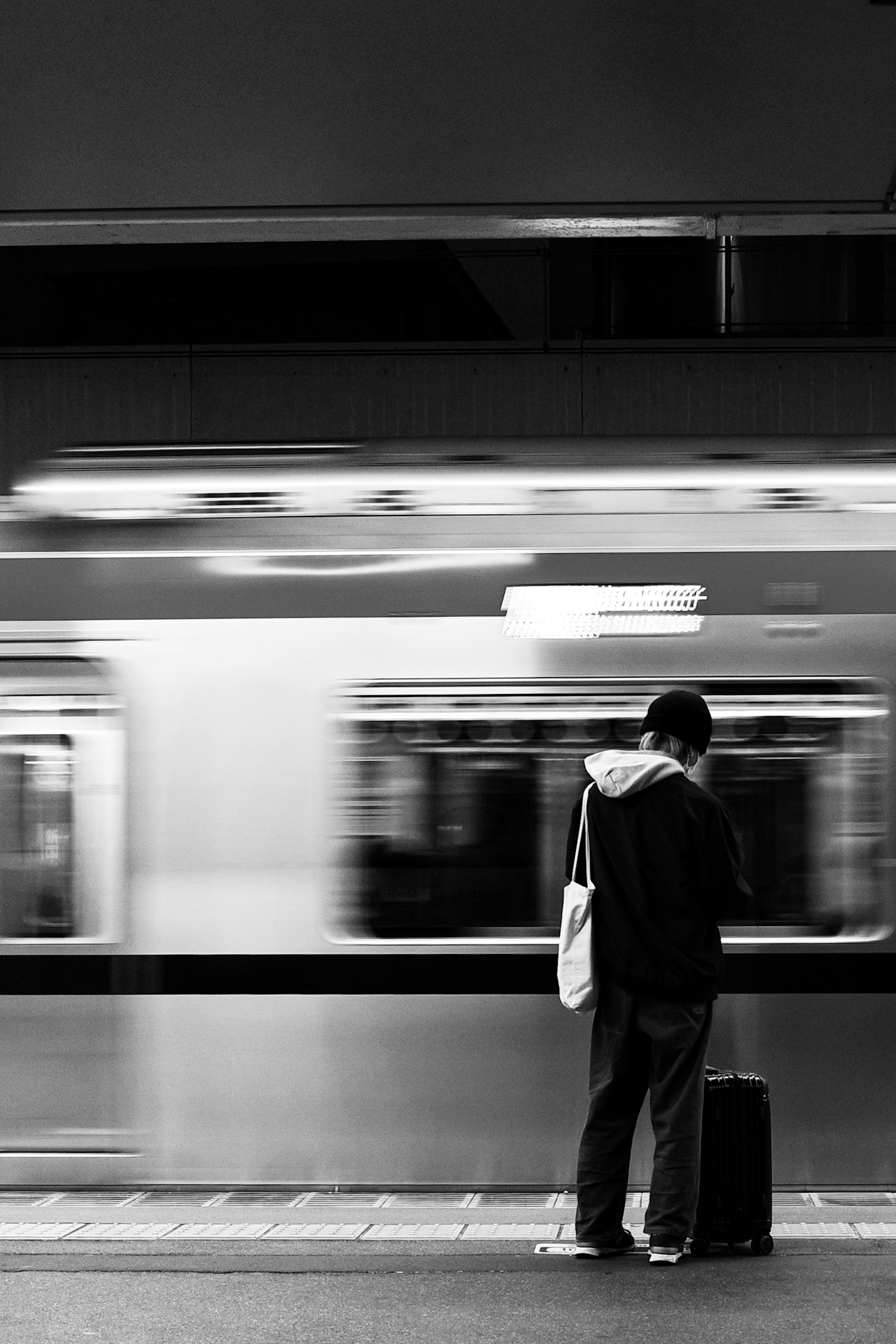 Une personne avec une valise attendant à une gare en noir et blanc