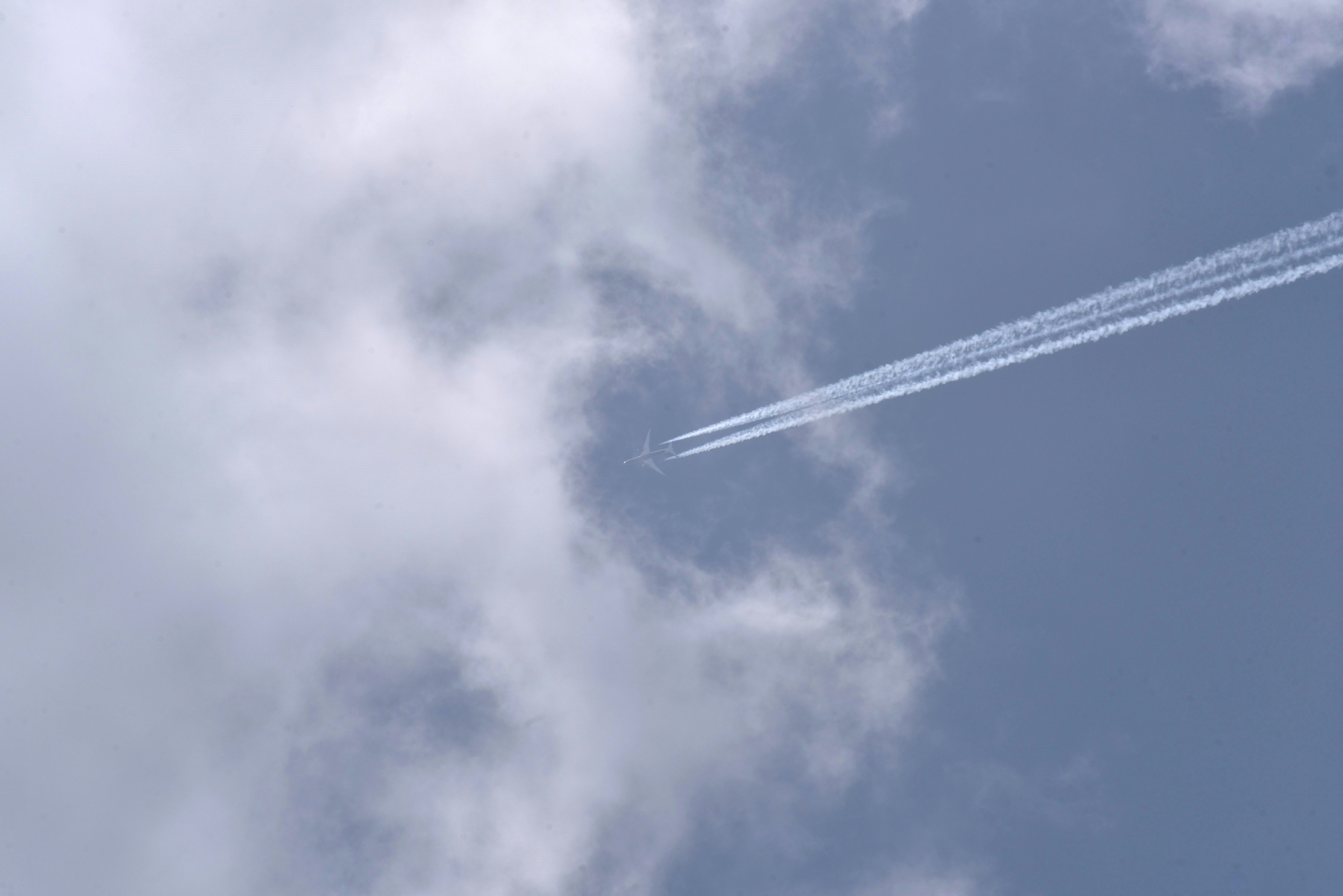 Kondensstreifen eines Flugzeugs im blauen Himmel zwischen Wolken sichtbar