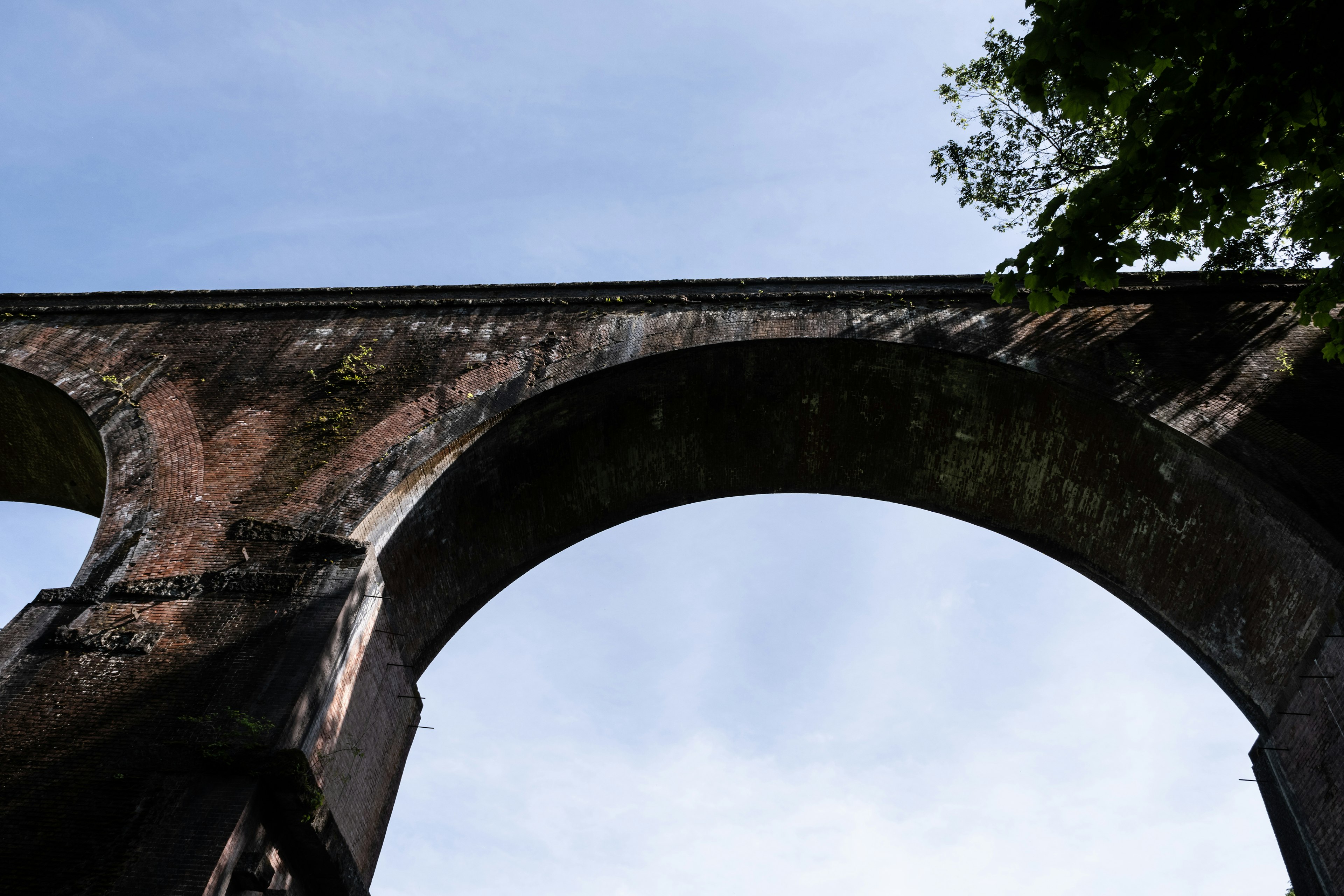 Vista da sotto un antico ponte ad arco in mattoni con cielo blu e alberi visibili