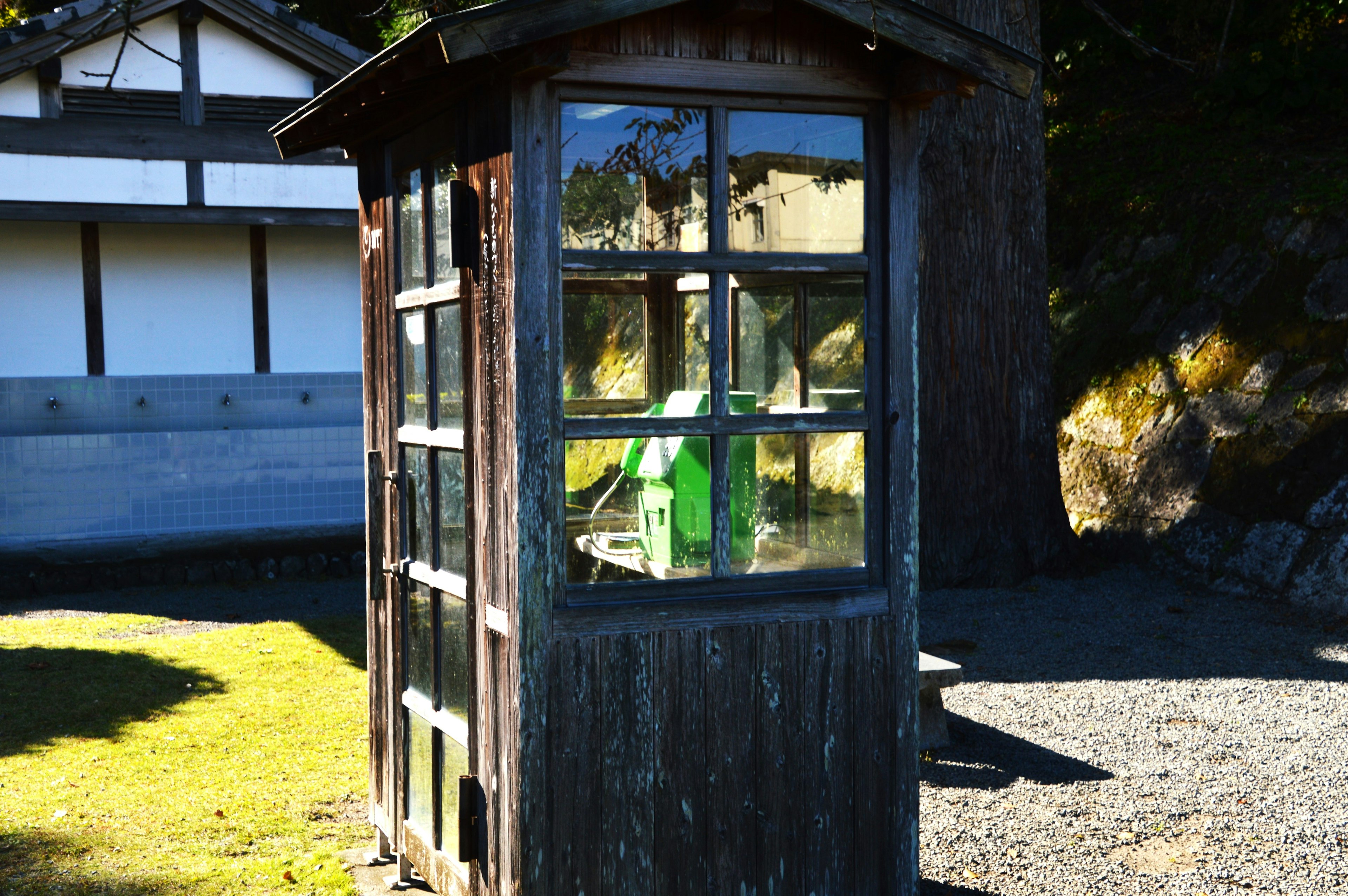 Una vecchia cabina telefonica in legno che riflette una sedia verde