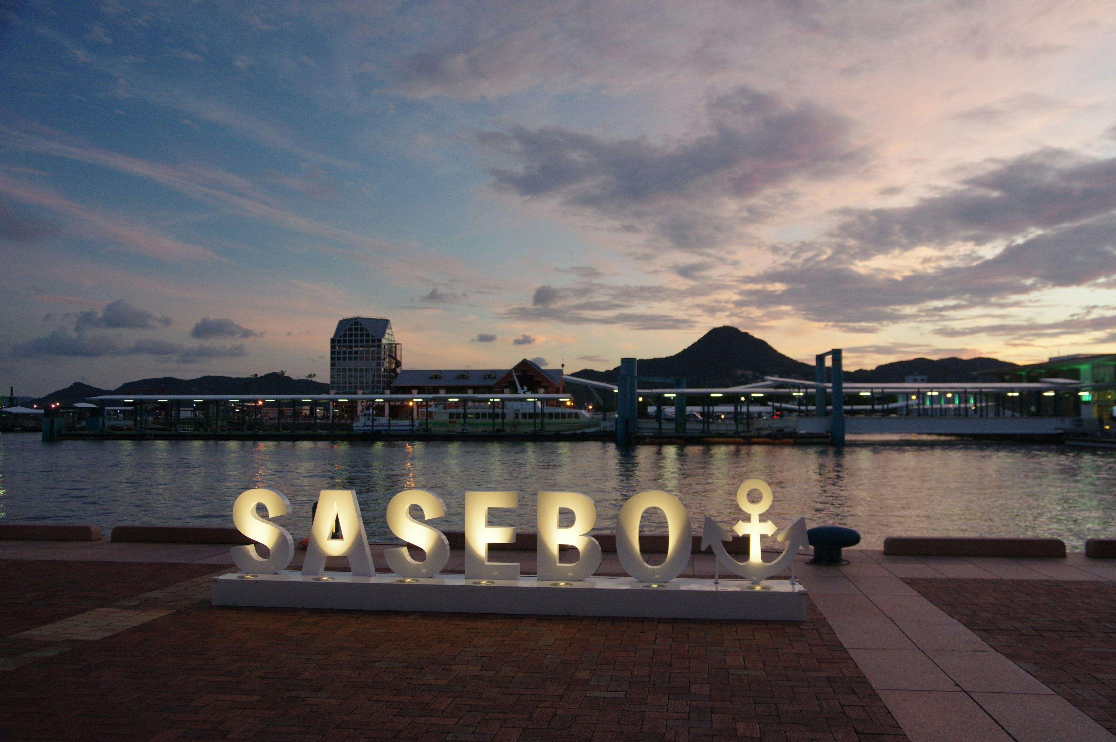 Pemandangan malam pelabuhan Sasebo dengan papan nama Sasebo dan simbol yang menyala