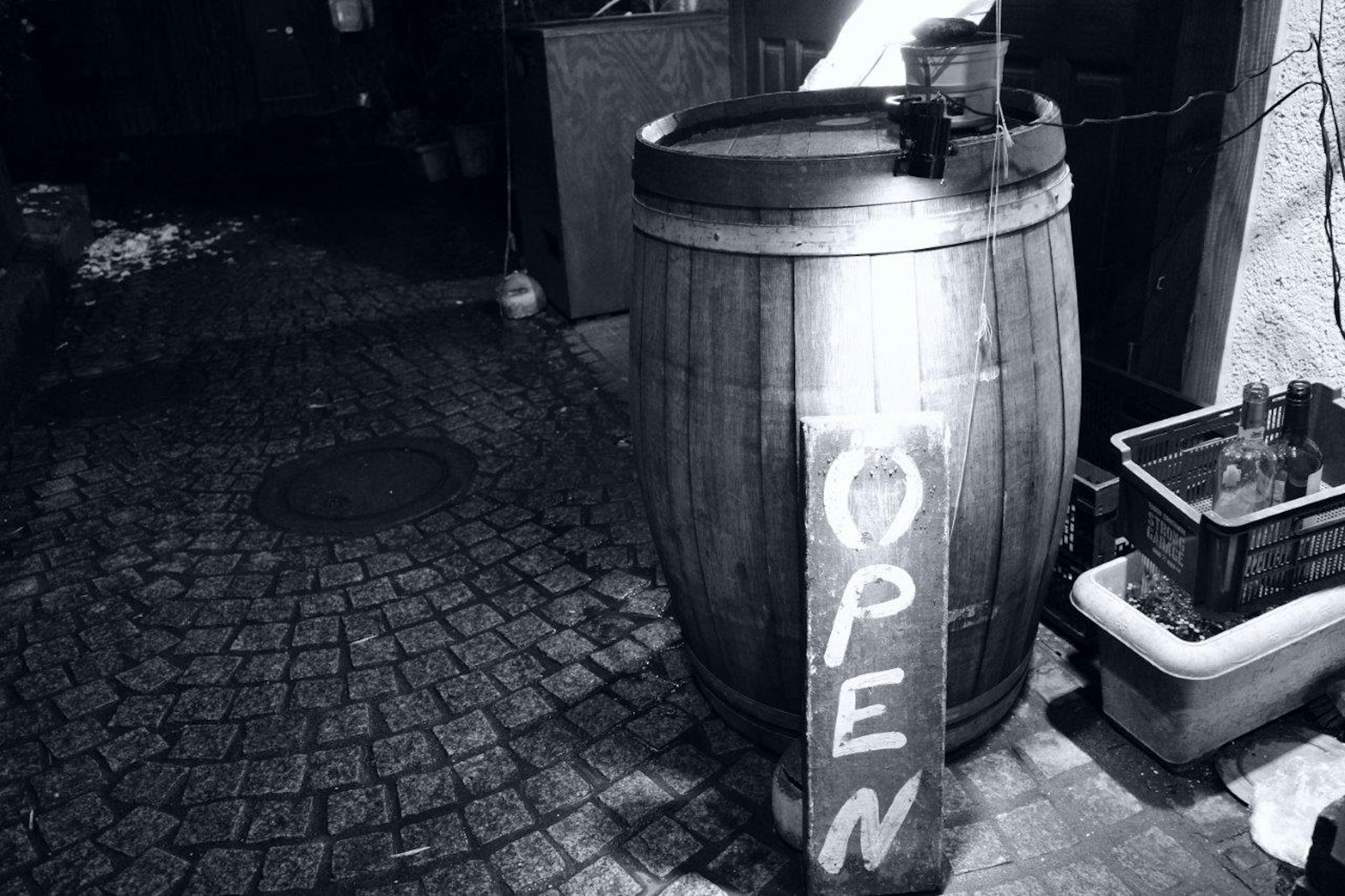 Barril de madera con un letrero 'OPEN' en un callejón nocturno