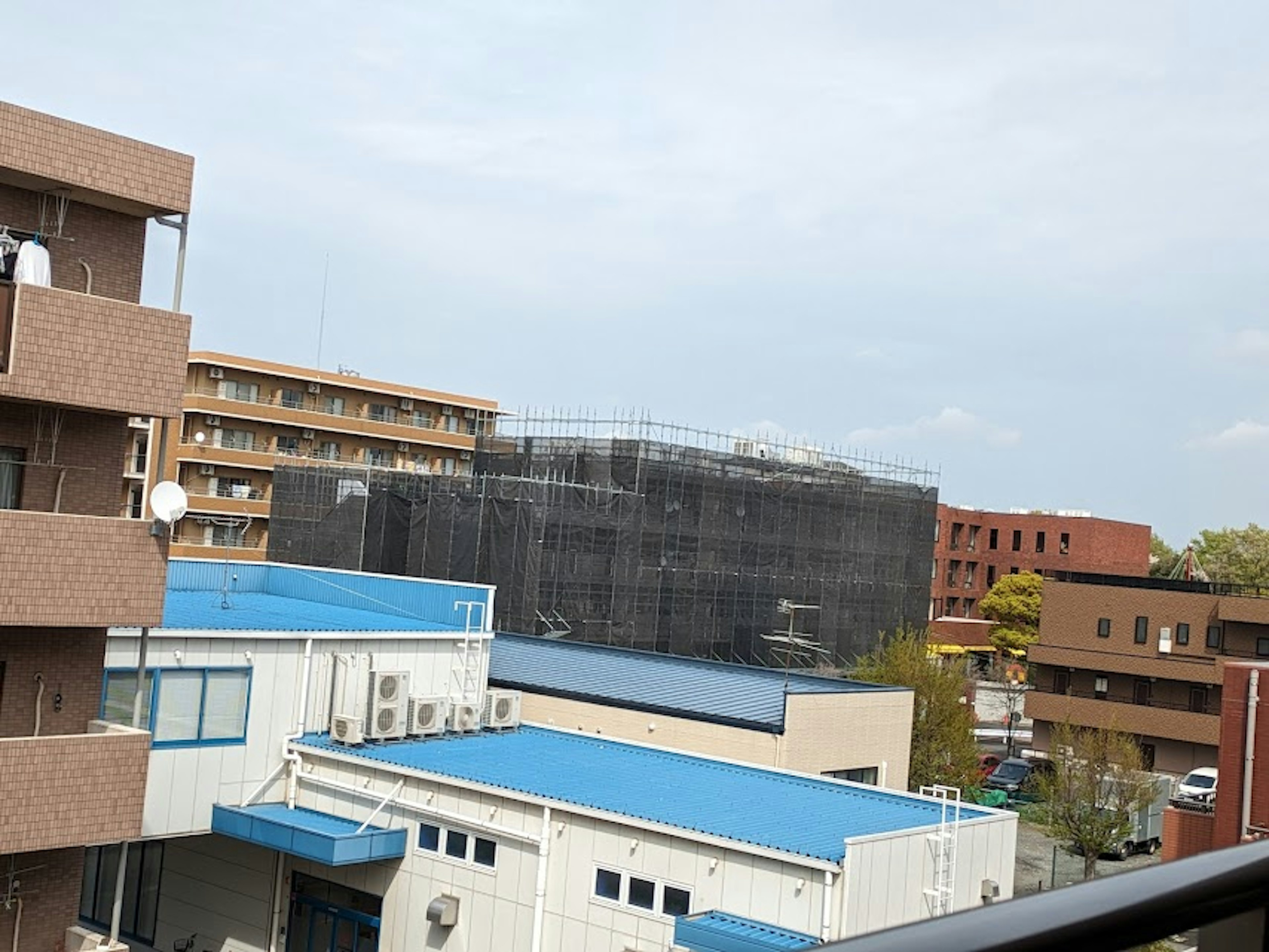 View of a construction site with a building covered in black netting blue-roofed structures and a cloudy sky