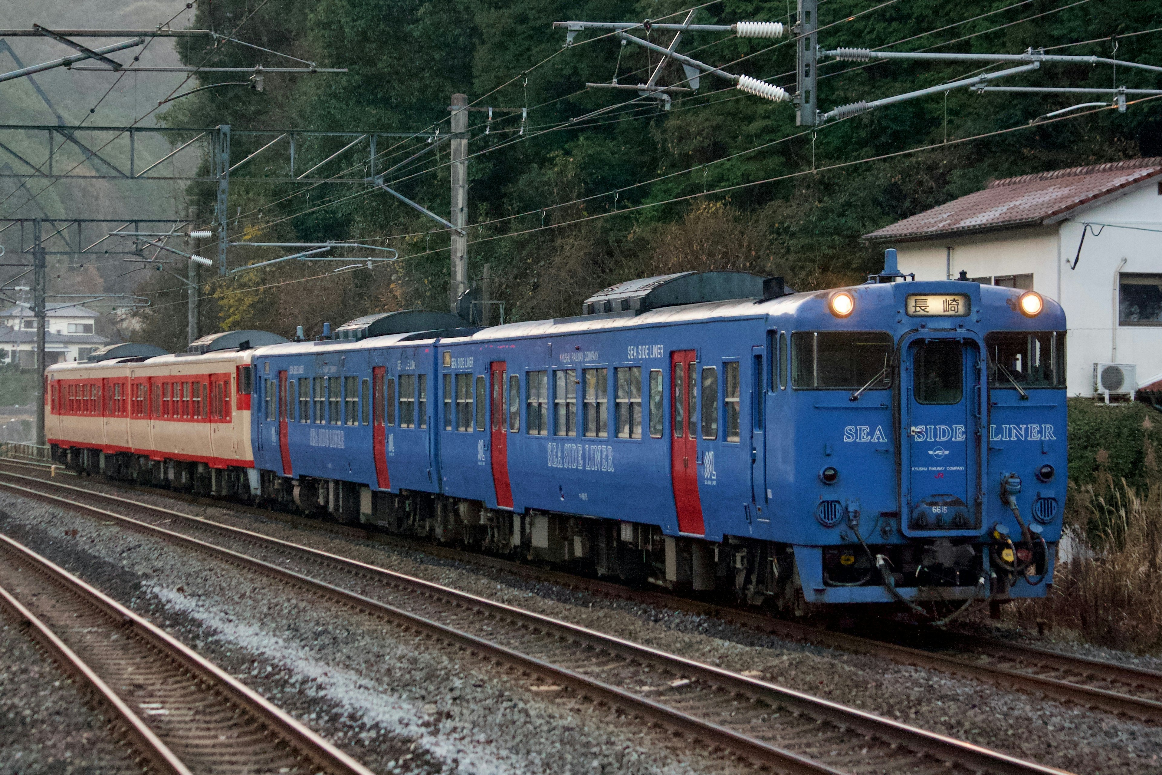 Blauer Zug fährt entlang der Gleise in einer malerischen Gegend