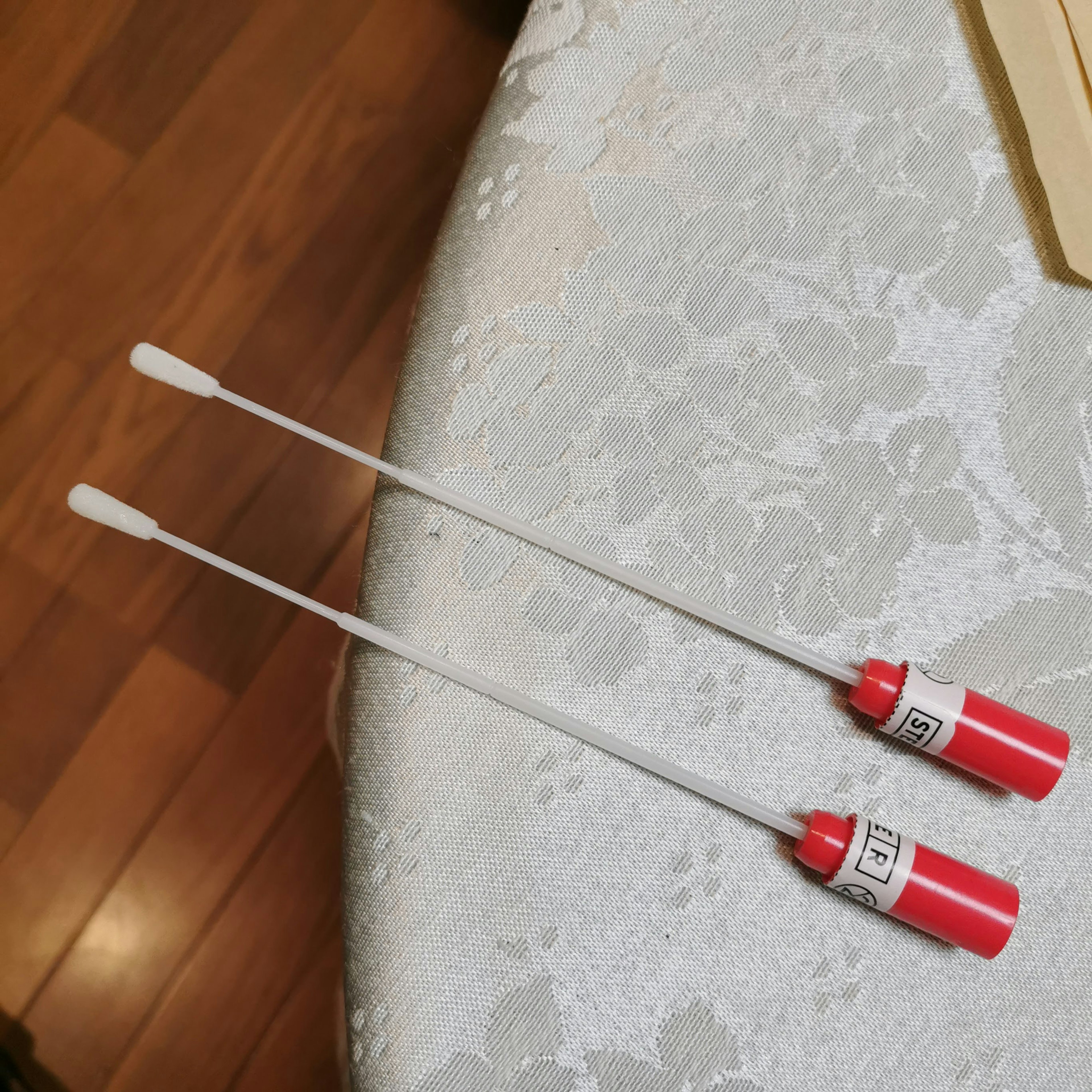 Two long white sticks with red caps lying on a light-colored surface