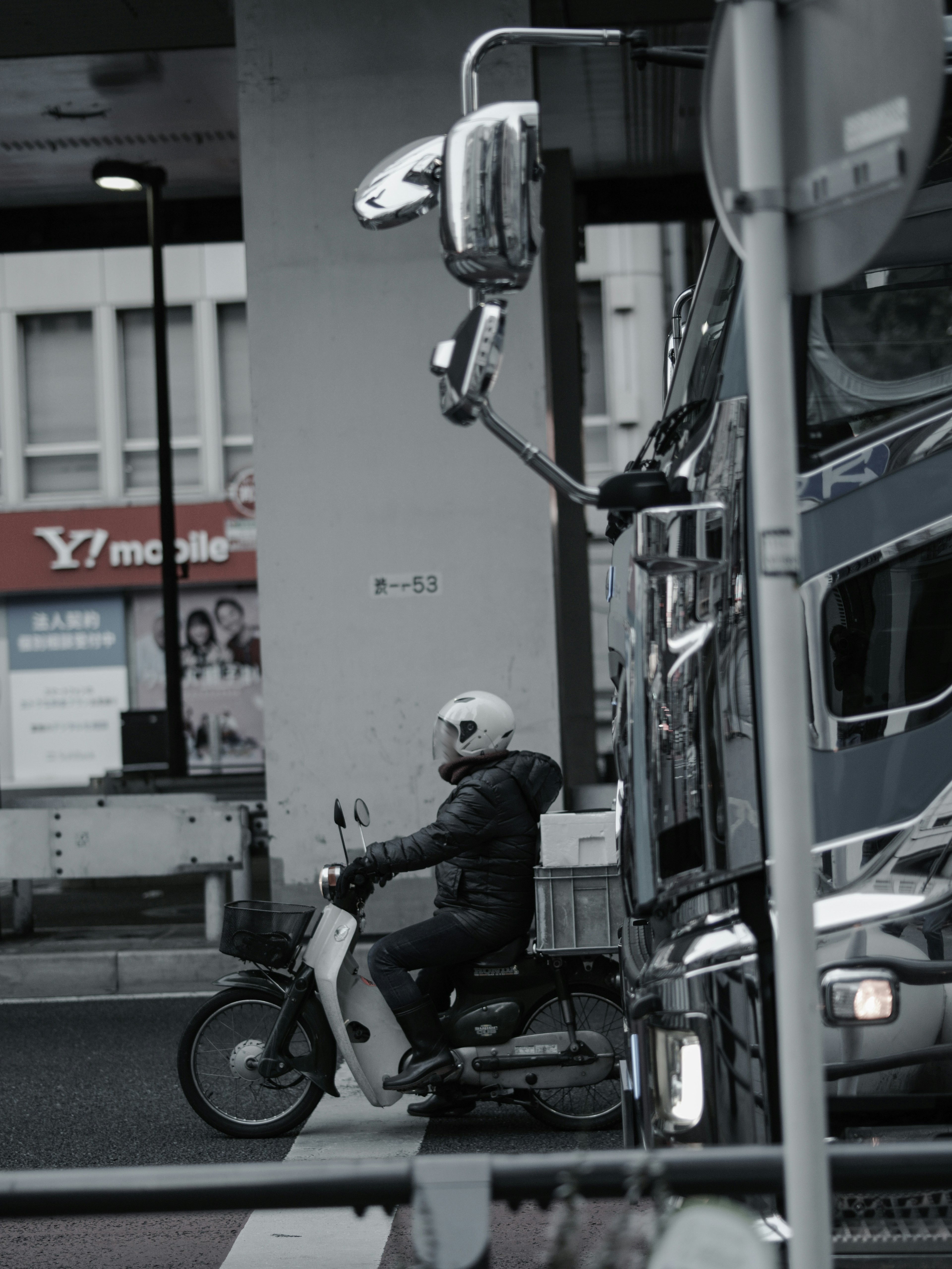 Un motard en casque blanc roulant sur une moto dans un paysage urbain monochrome