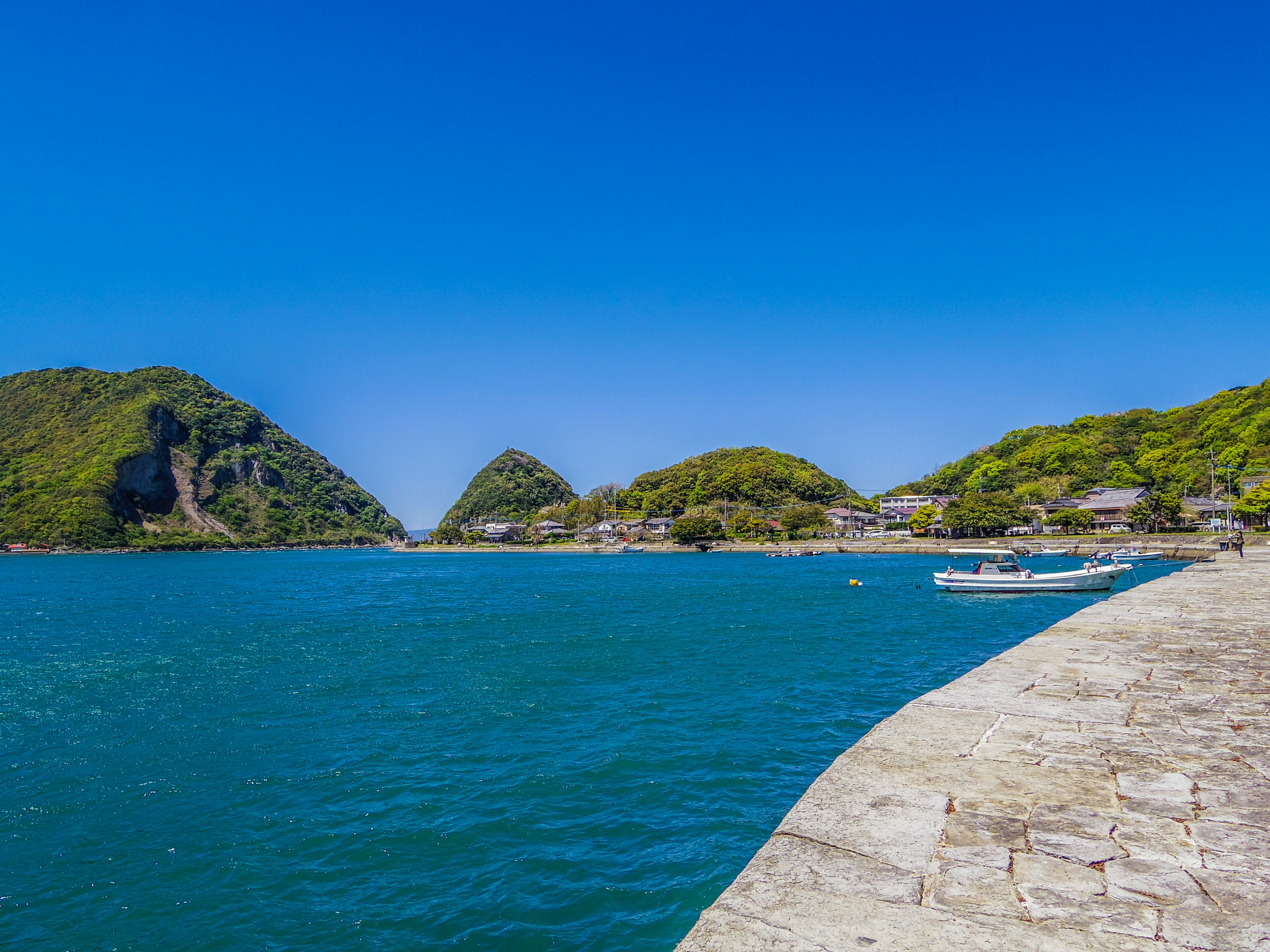 Scenic view of blue sea and green hills with boats at the harbor