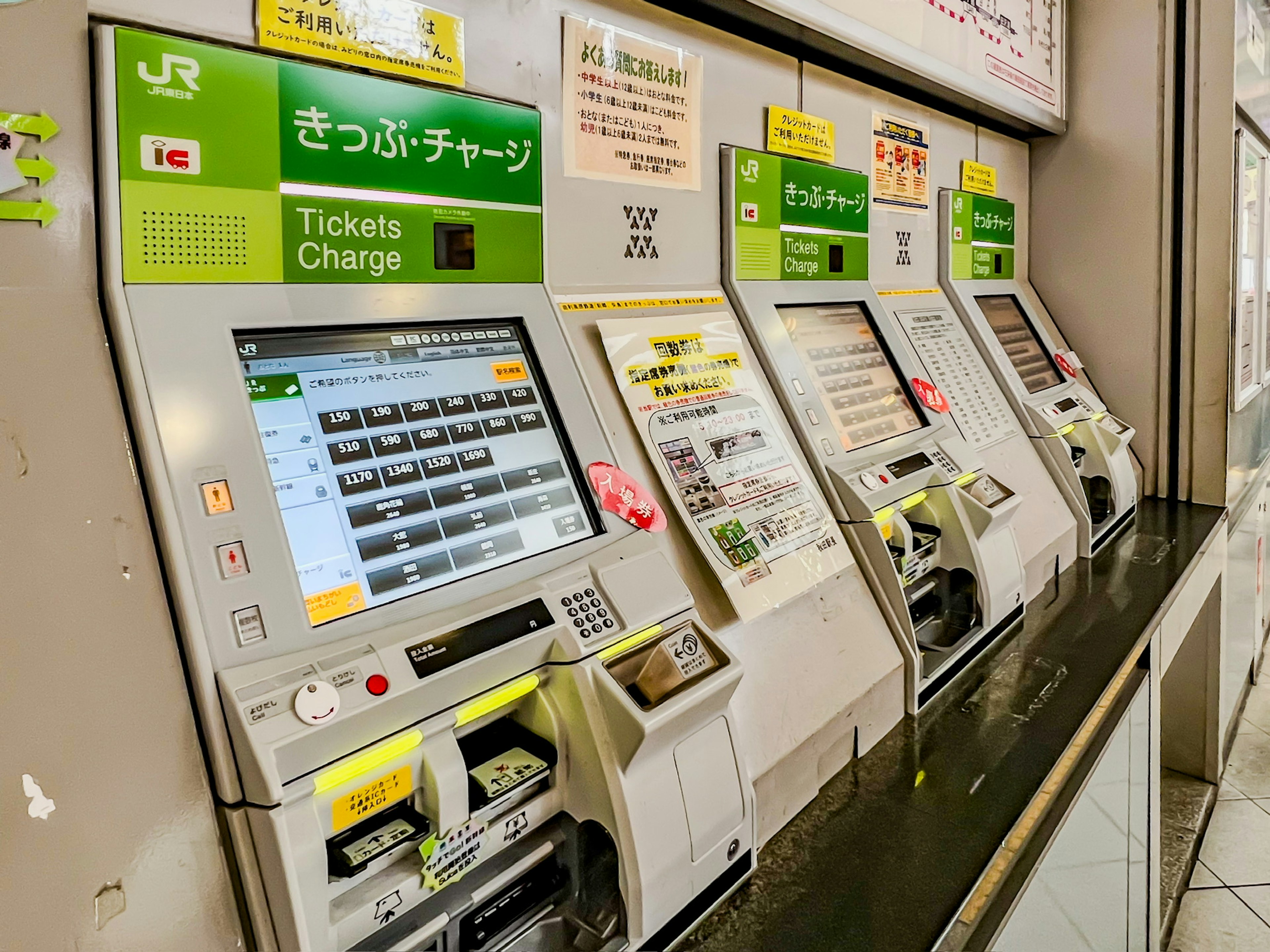 Fila di biglietterie automatiche in una stazione con schermi in giapponese e inglese