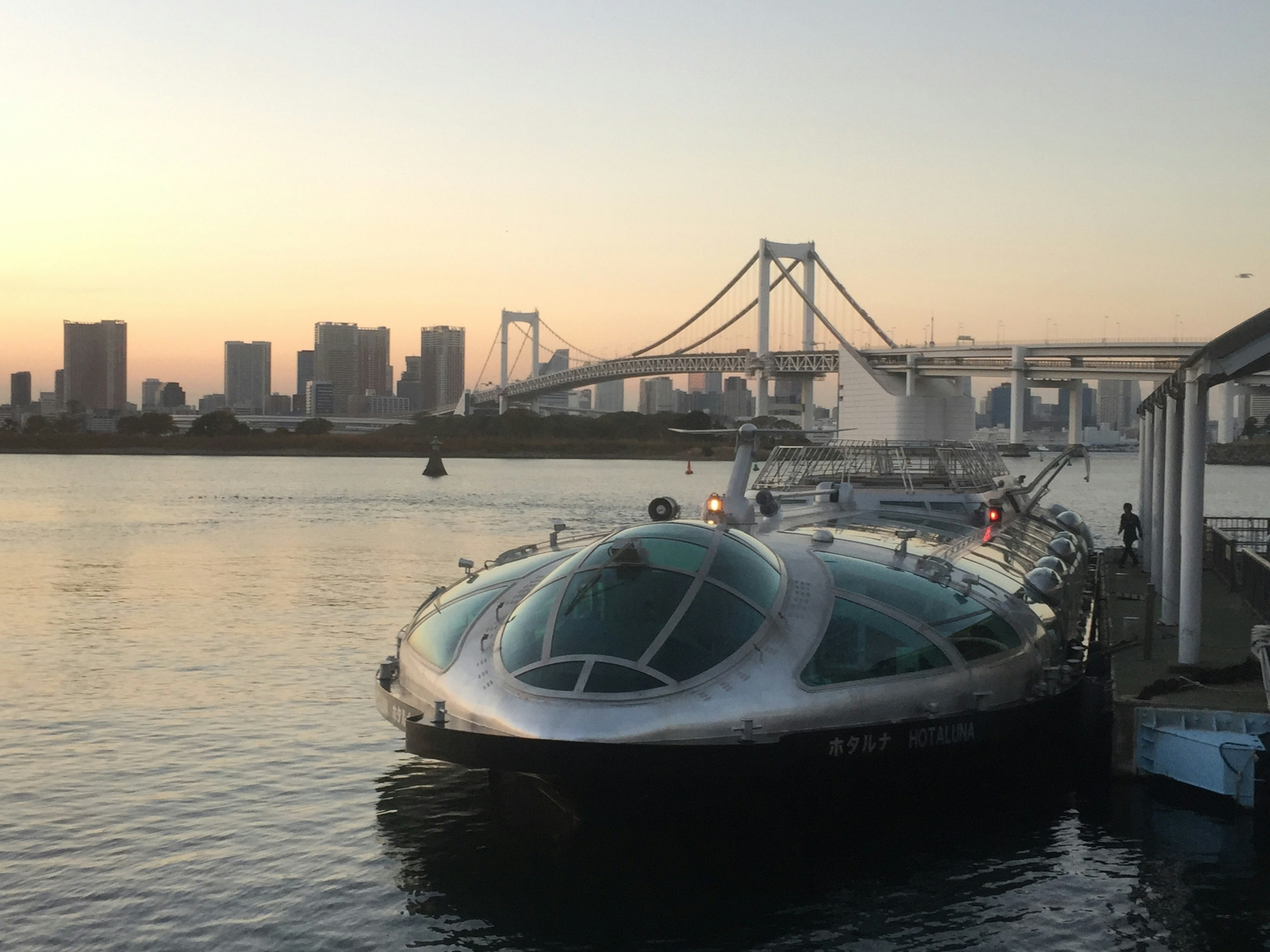 Futuristisches Boot in der Bucht von Tokio mit der Rainbow Bridge bei Sonnenuntergang