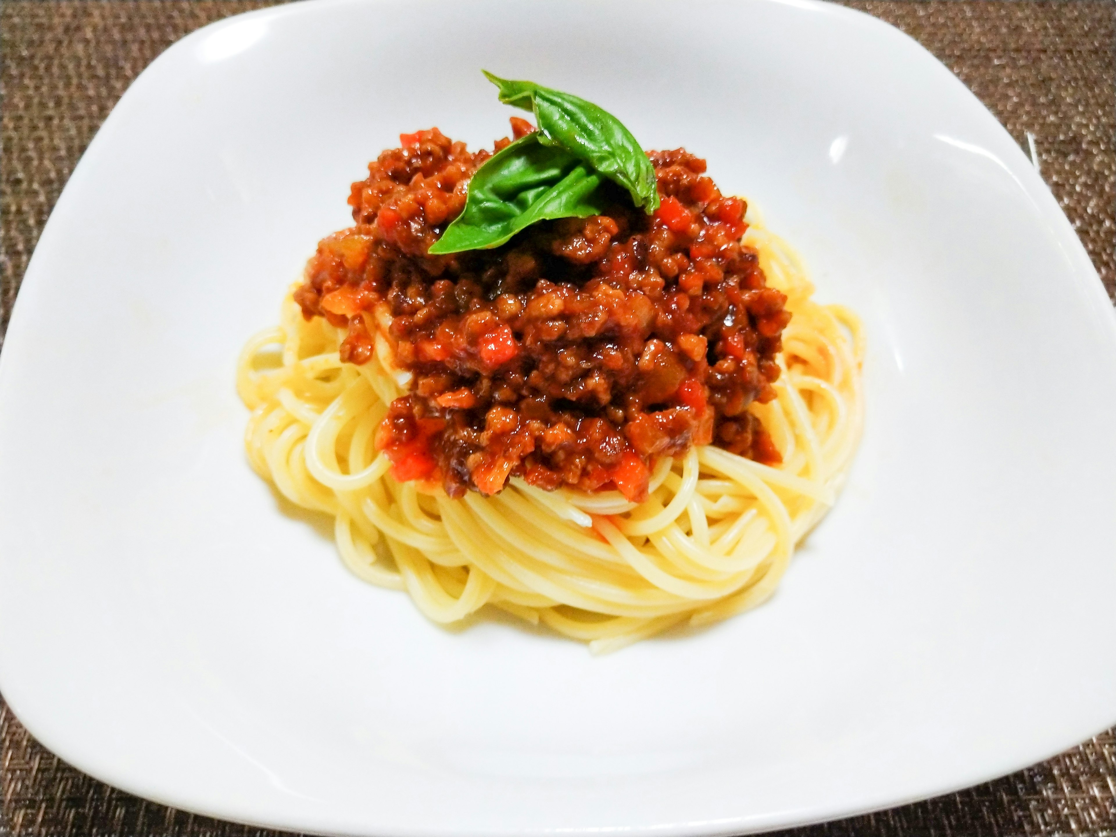 Spaghetti Bolognese served on a white plate with fresh basil