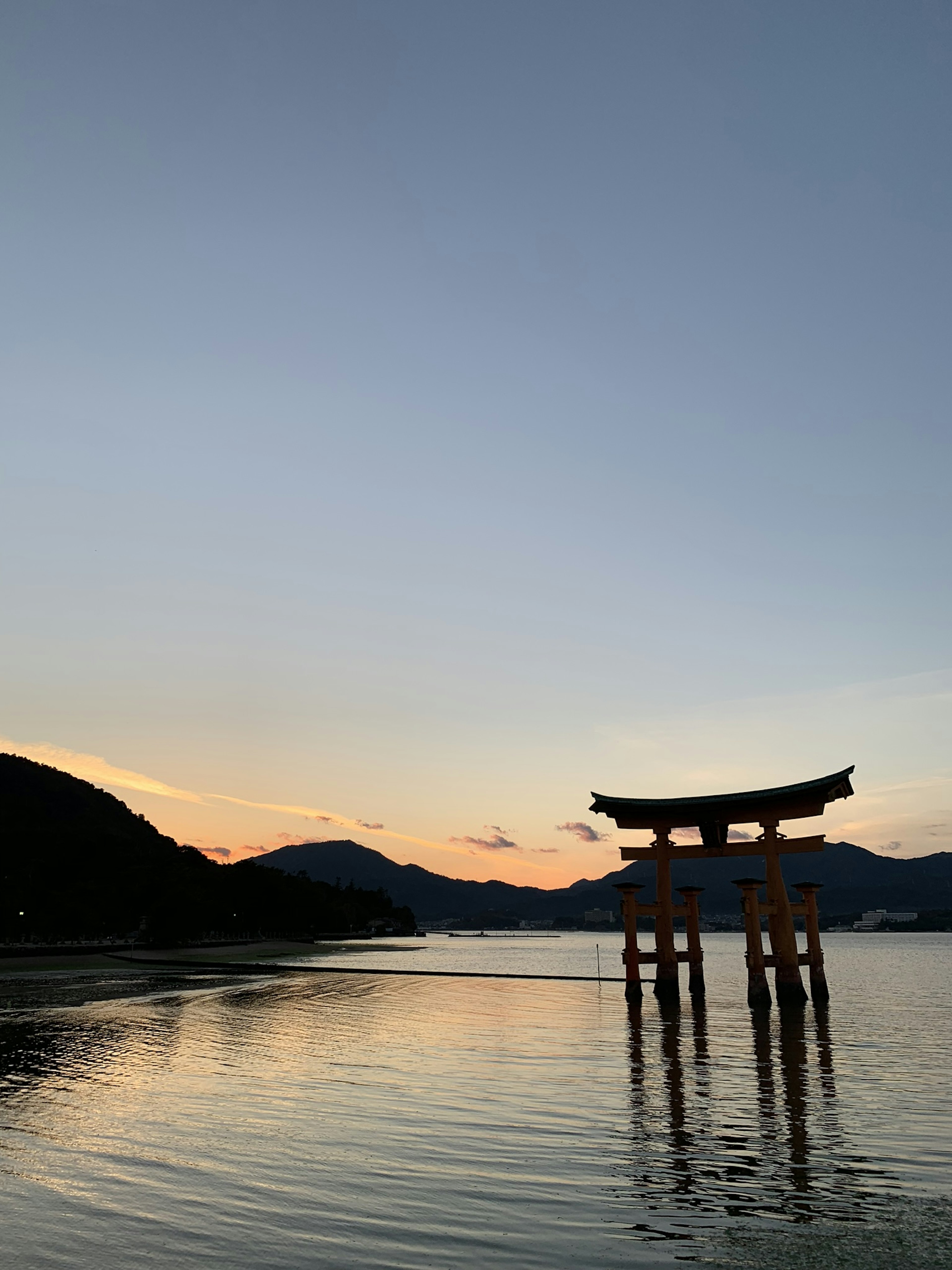 Siluet gerbang torii saat matahari terbenam dengan pantulan di air