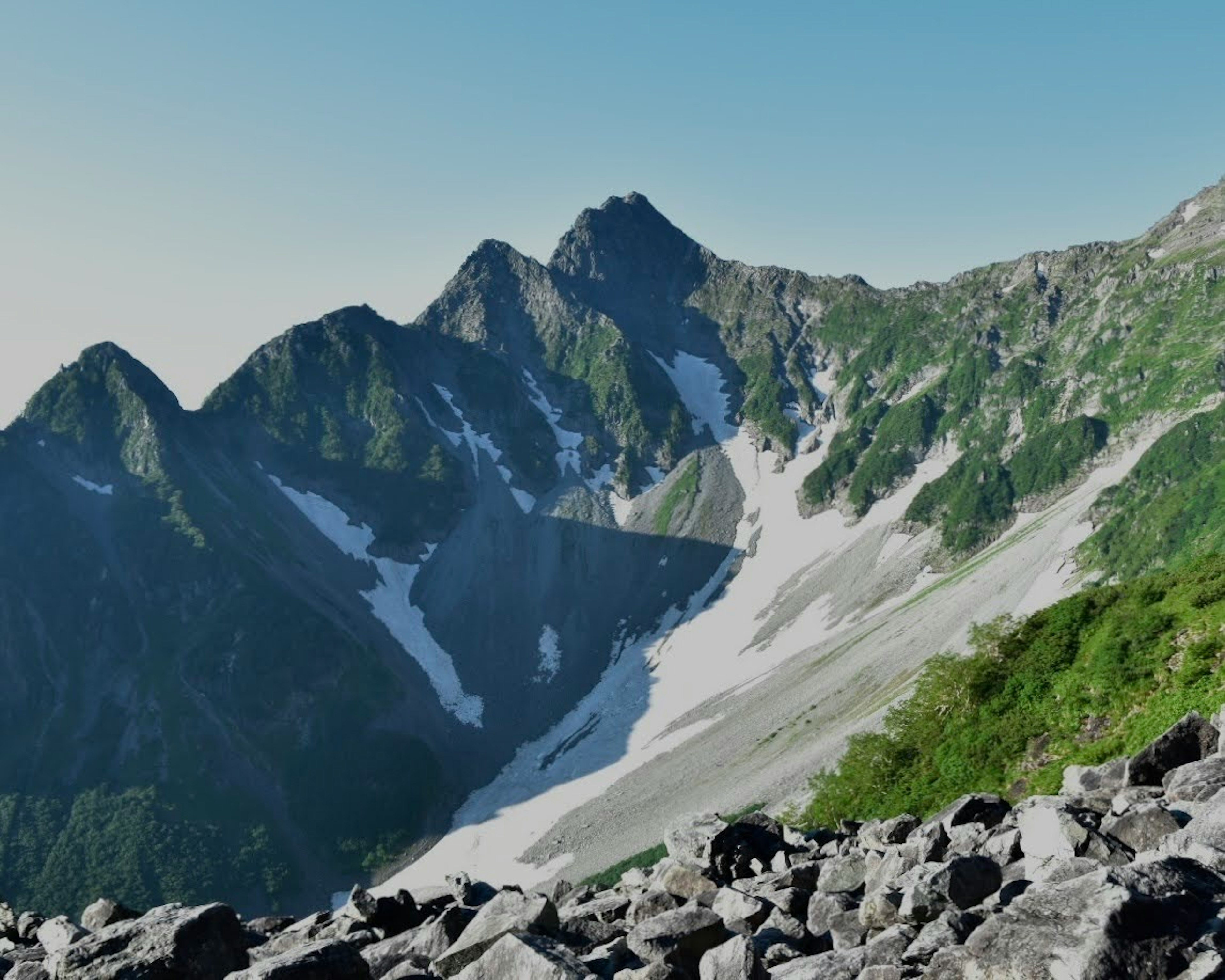 美しい山脈の風景、雪の残る斜面と緑の植生、岩の多い地面