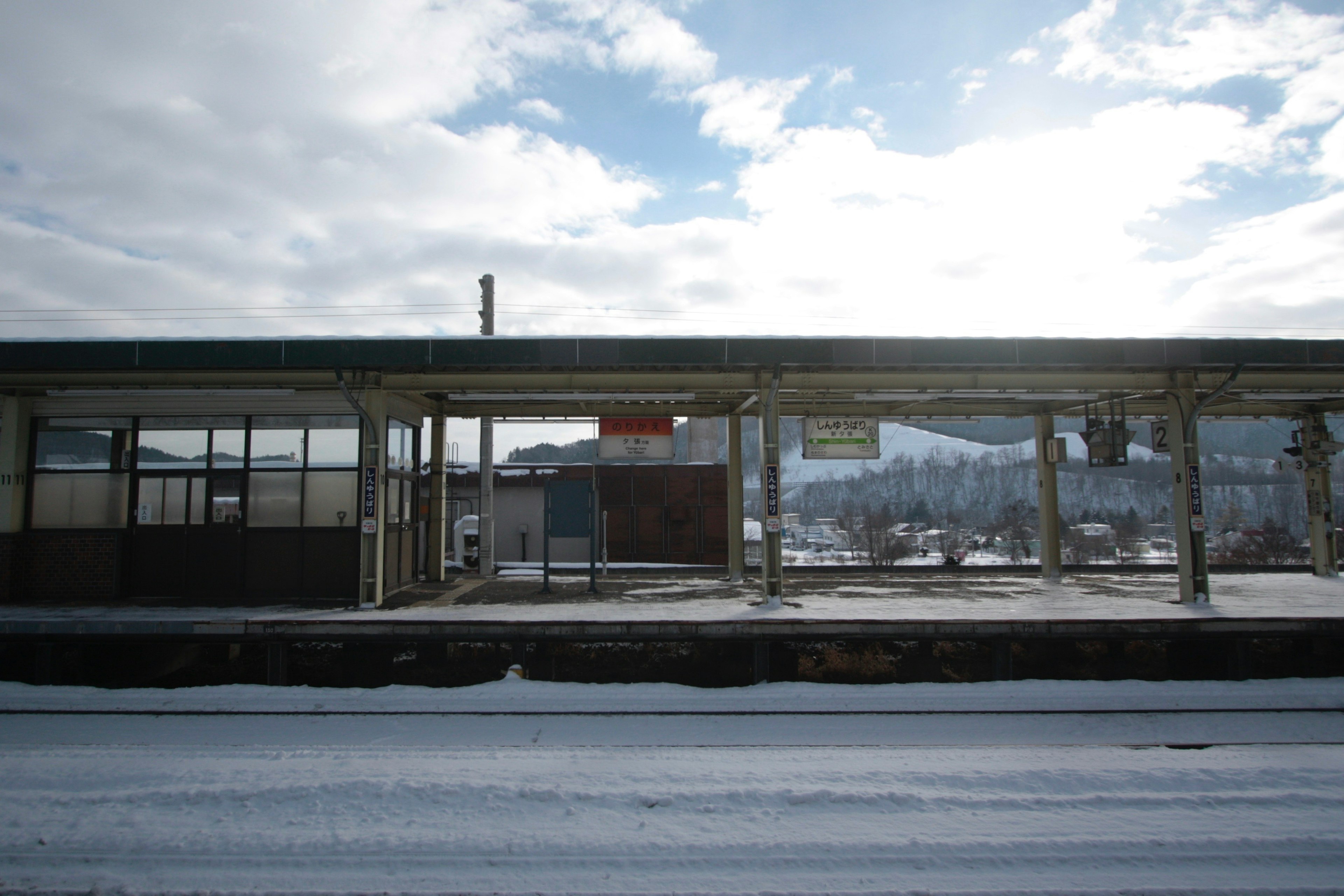 Schneebedeckter Bahnhof mit blauem Himmel und Bergen im Hintergrund