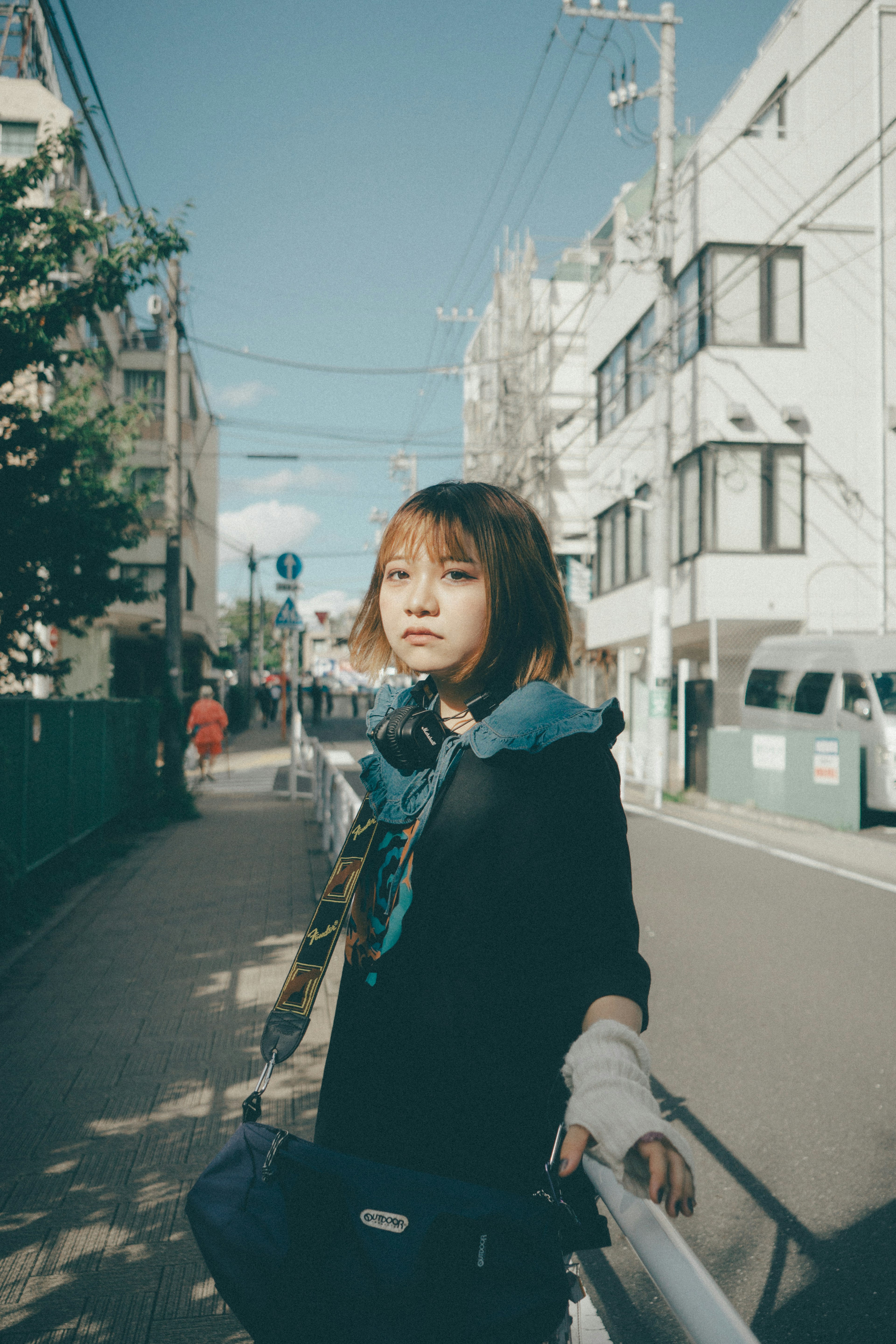 A girl posing on a city street wearing a blue scarf and black clothing with a slightly blurred background