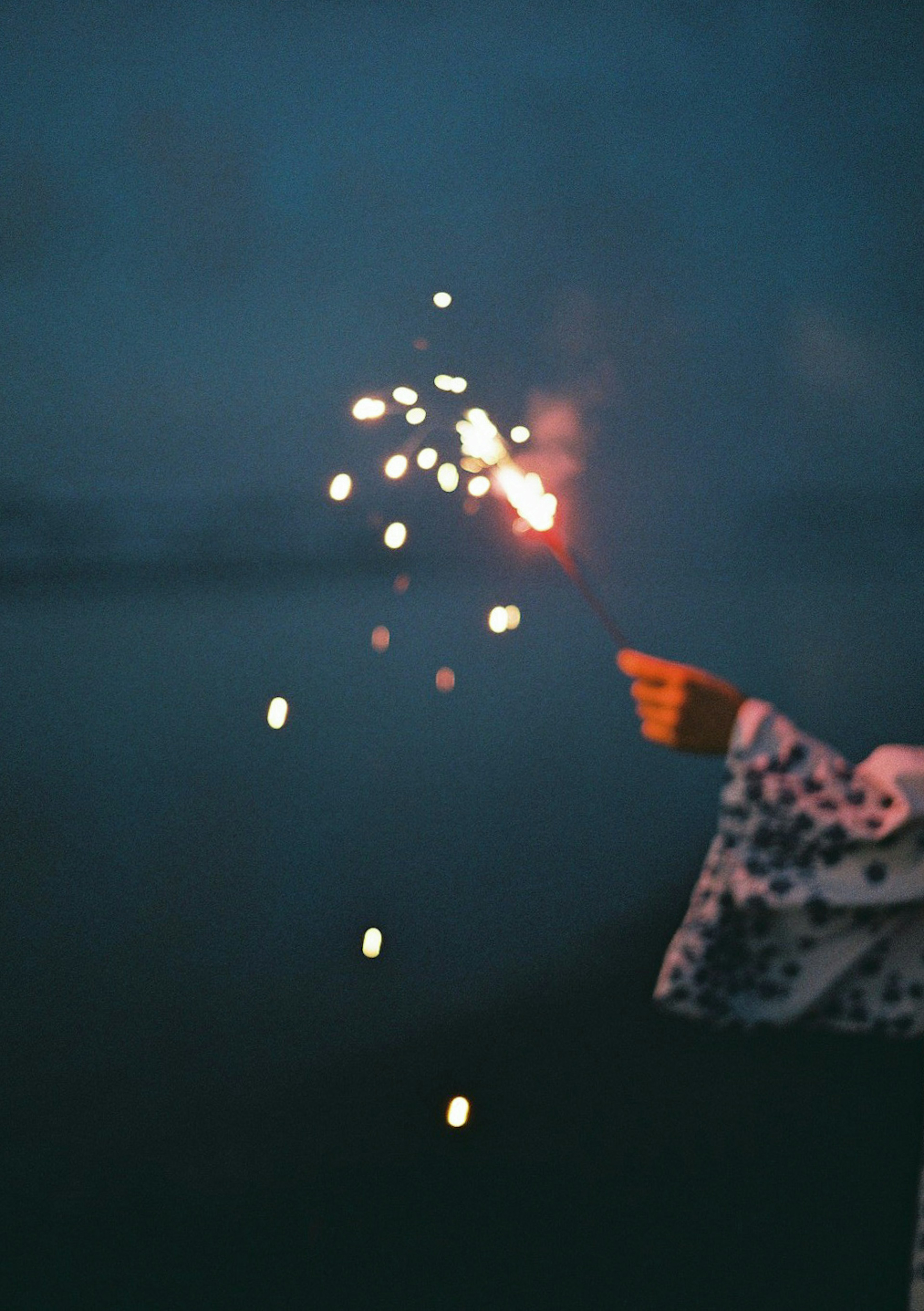 A person's hand holding a sparkler against a dark background