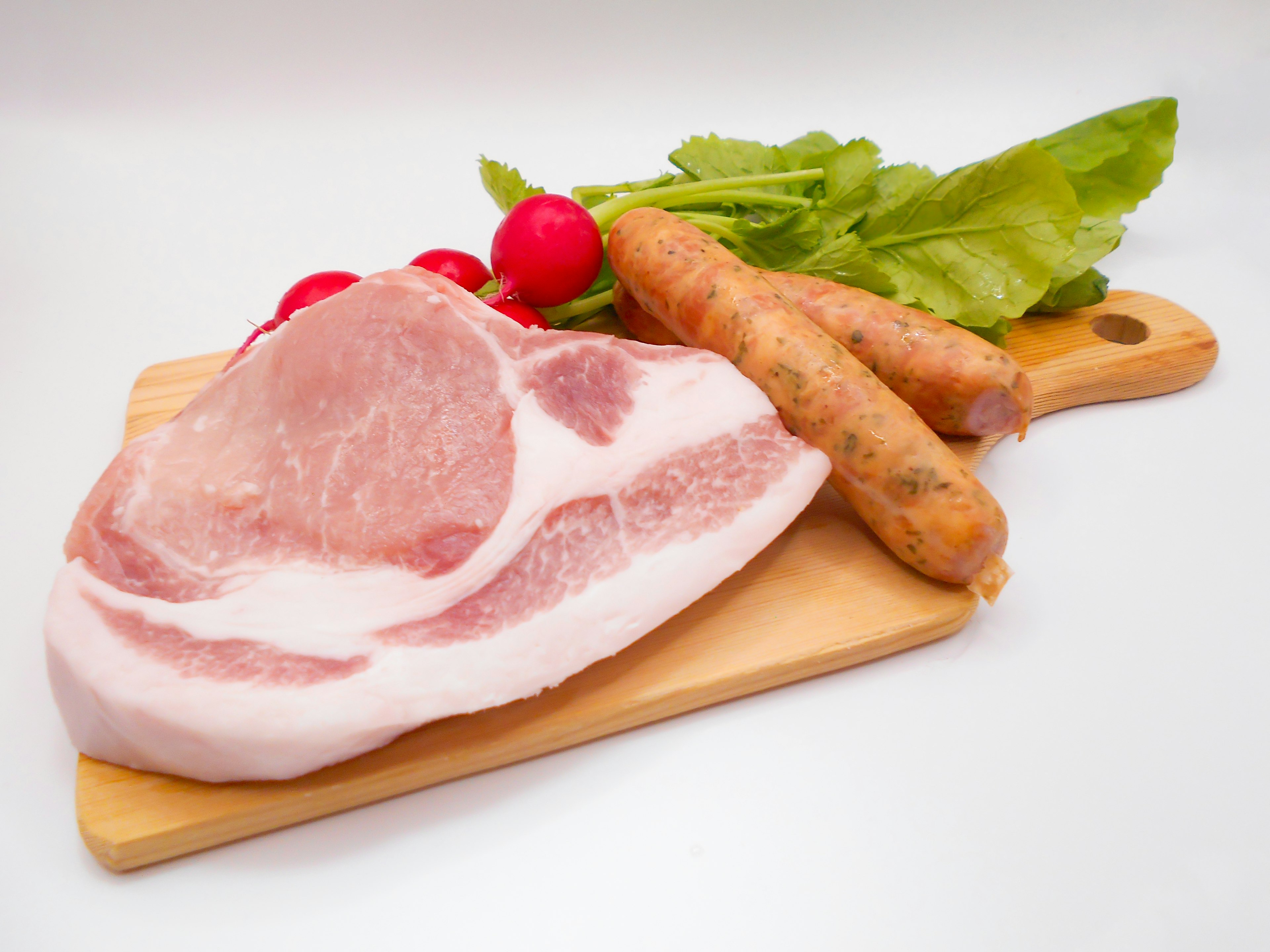 Tranche de porc, saucisses, radis et feuilles de menthe disposés sur une planche à découper en bois