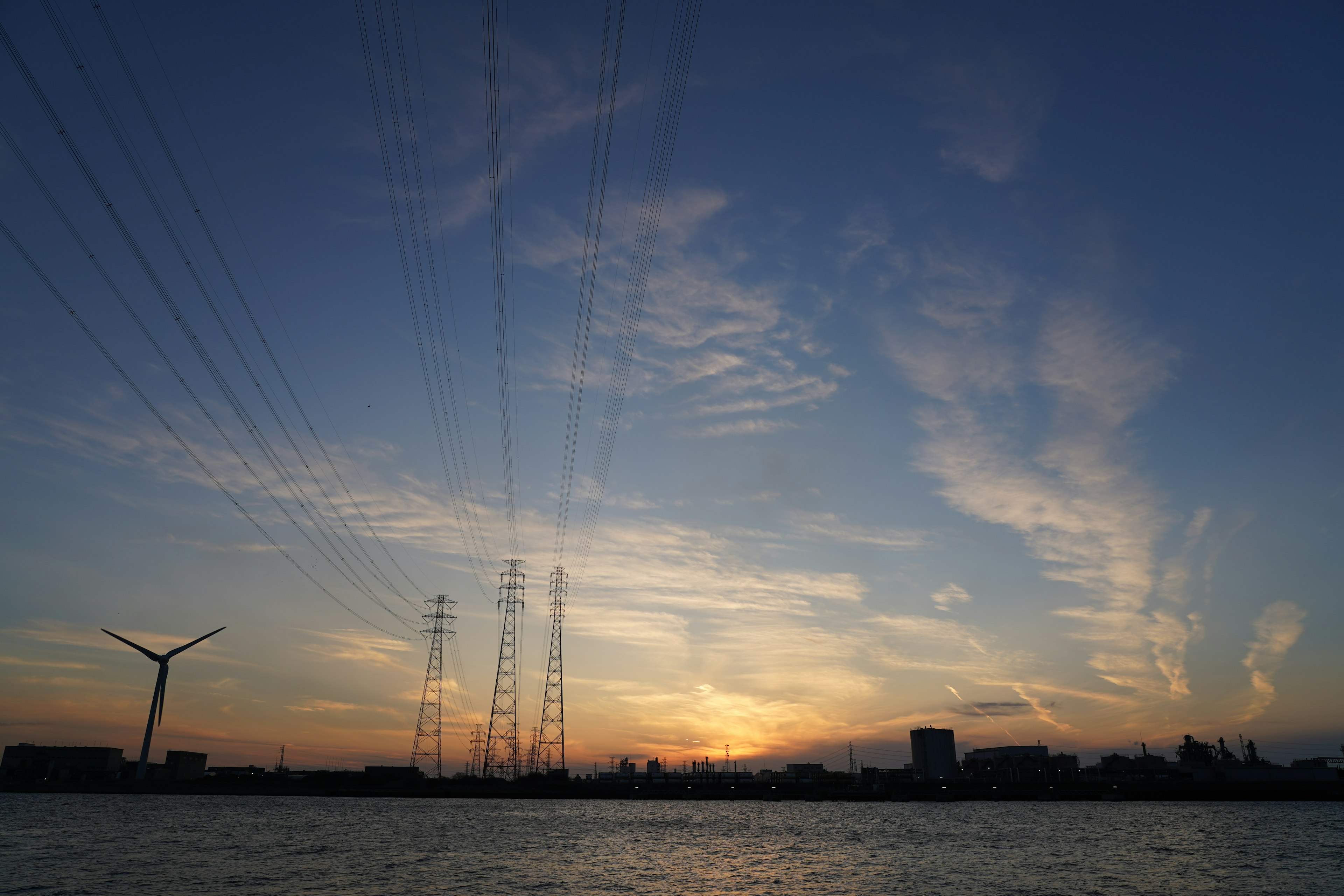 Wunderschöner Sonnenuntergang mit sich kreuzenden Stromleitungen und einer Windkraftanlage