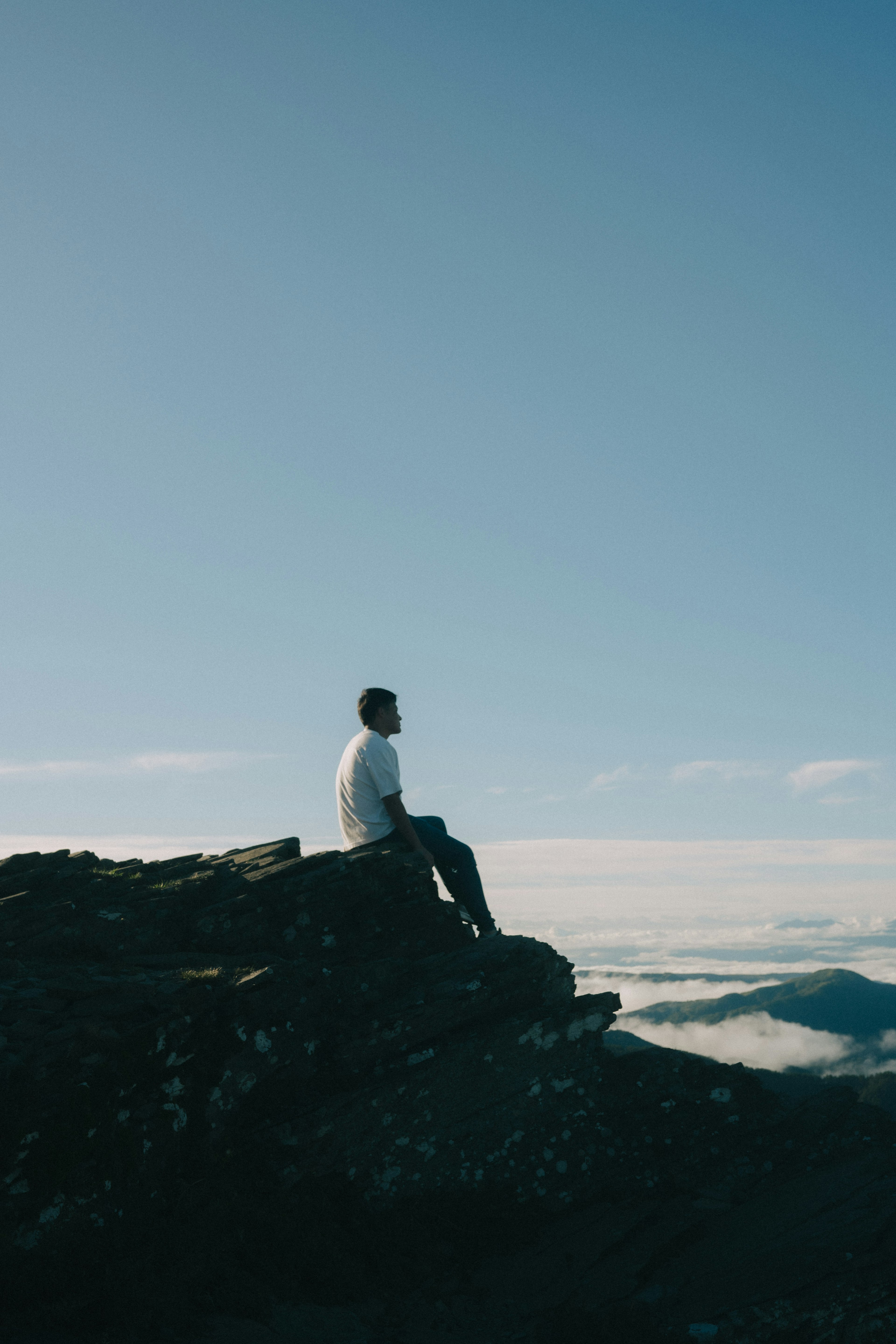 Mann, der ruhig auf einem Berggipfel sitzt, unter einem blauen Himmel