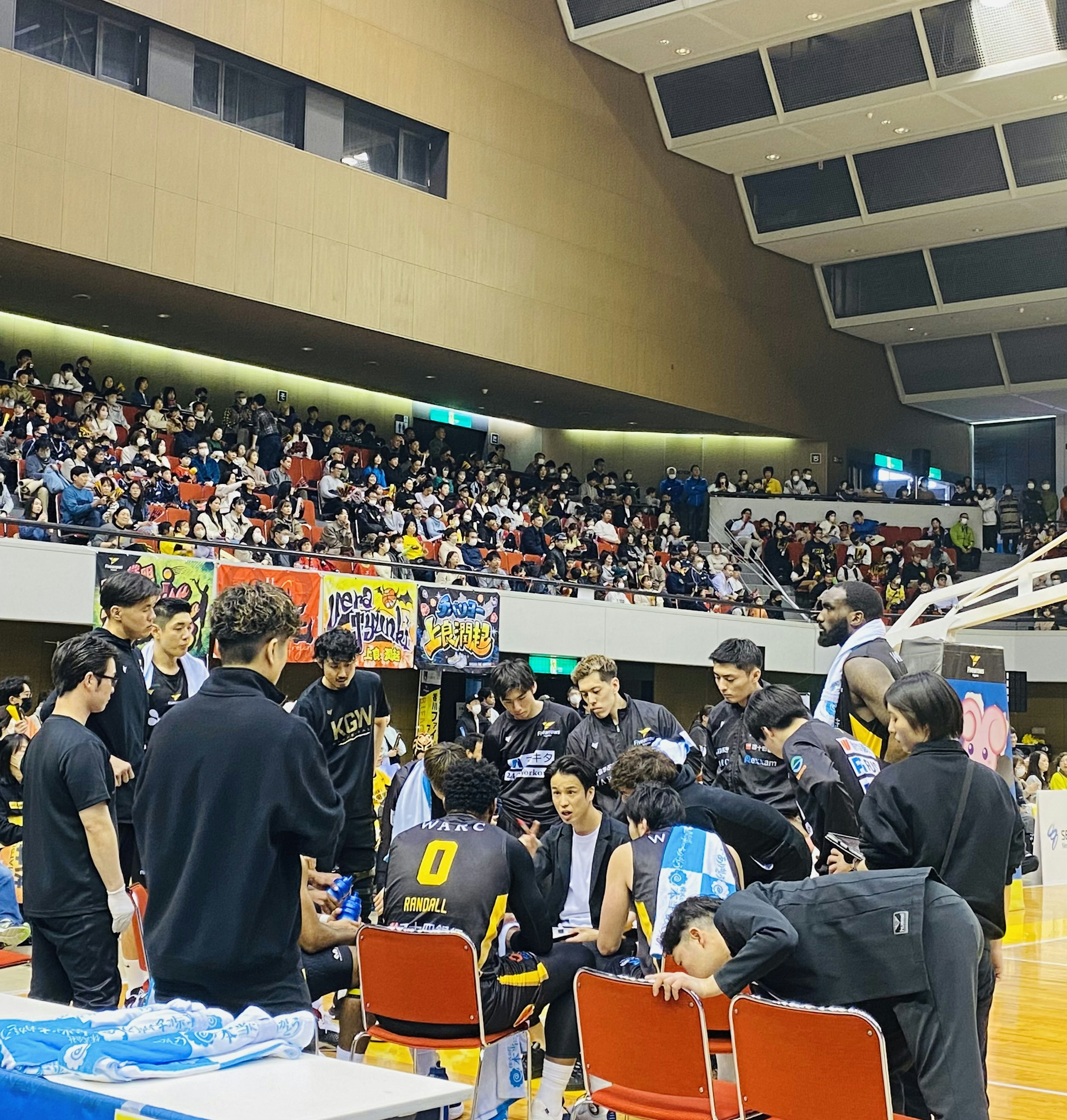 Squadra di basket che discute strategie durante una partita con uno stadio affollato