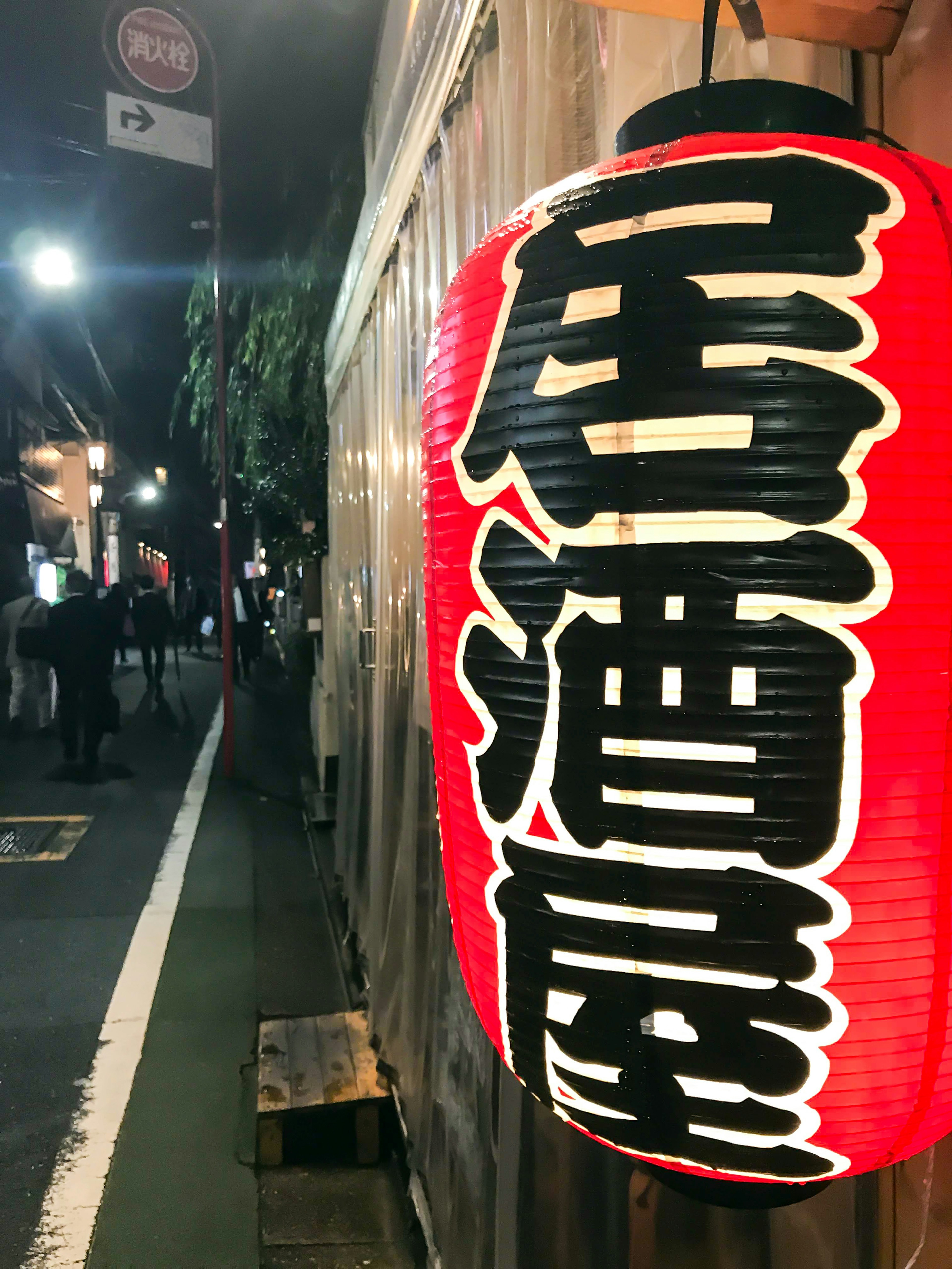 Lanterne rouge avec des caractères d'izakaya et une scène de rue nocturne