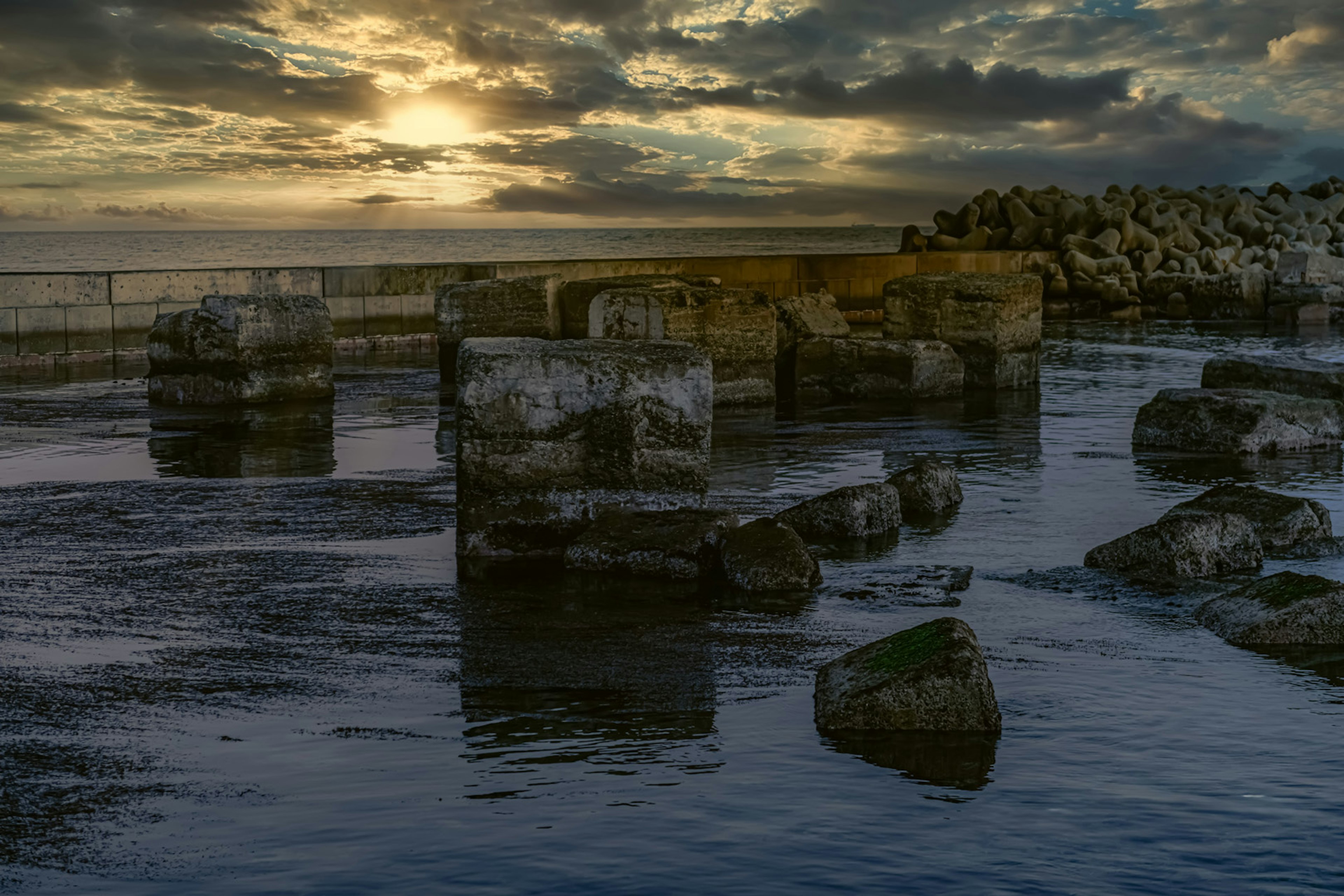 Stone structures partially submerged in water under a sunset sky