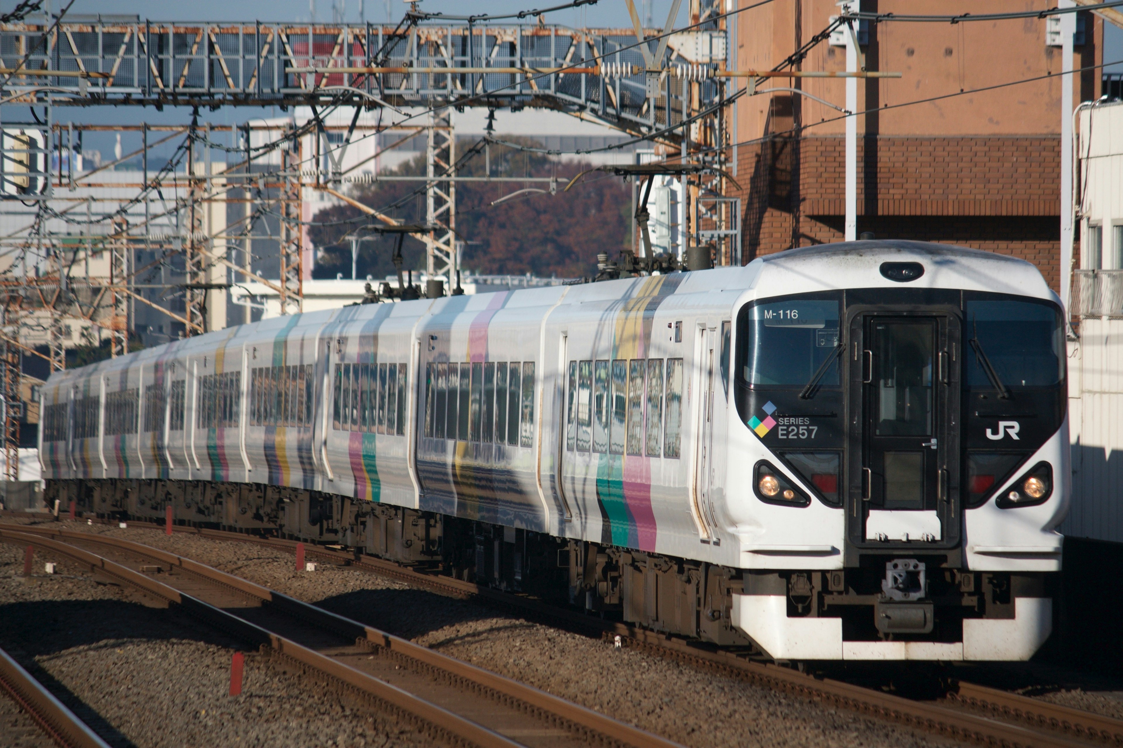 A white train running on tracks with a clear blue sky and buildings in the background