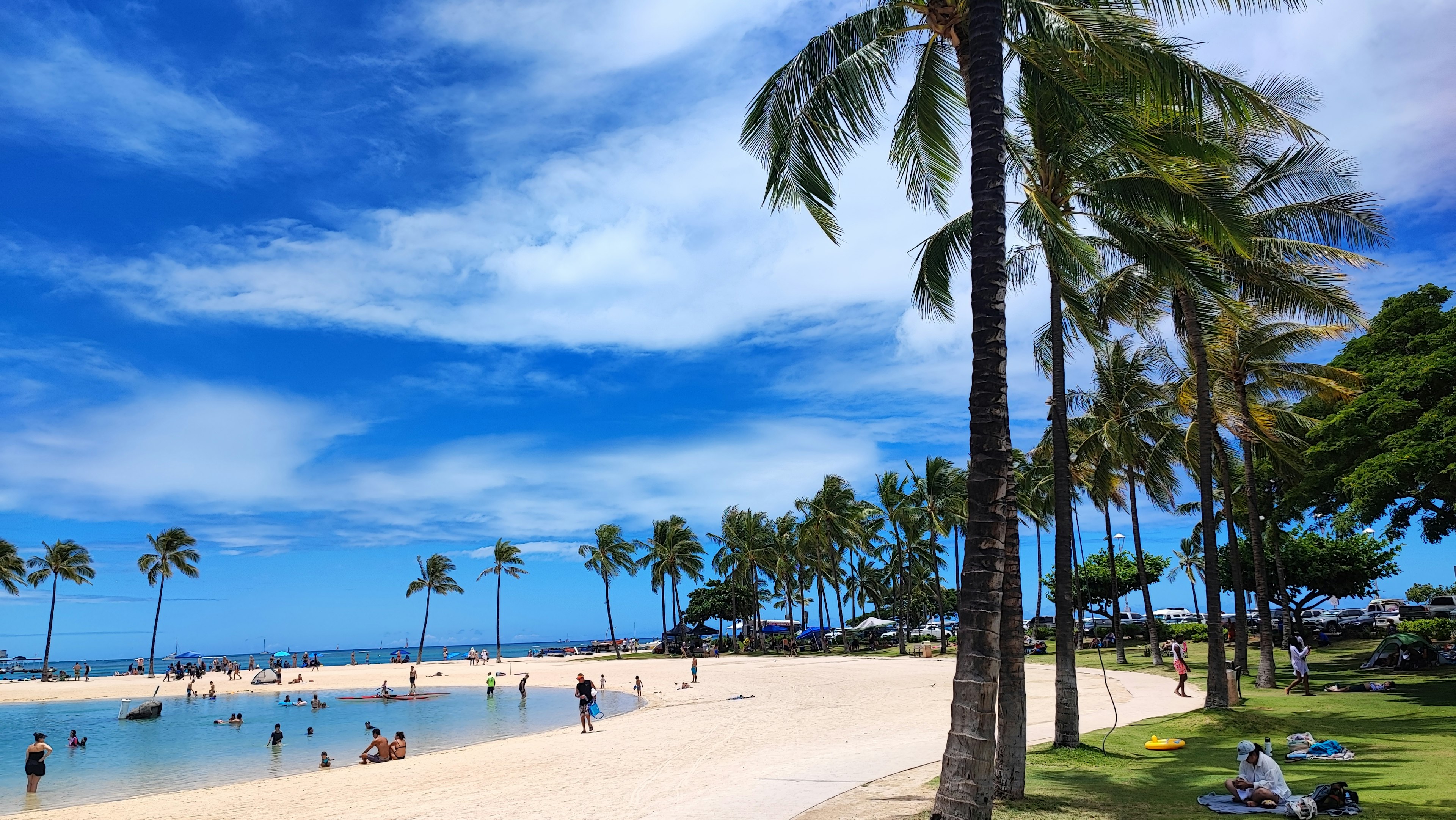 ทิวทัศน์ชายหาดท้องฟ้าสีฟ้าและทรายขาวผู้คนกำลังสนุกสนานในน้ำ