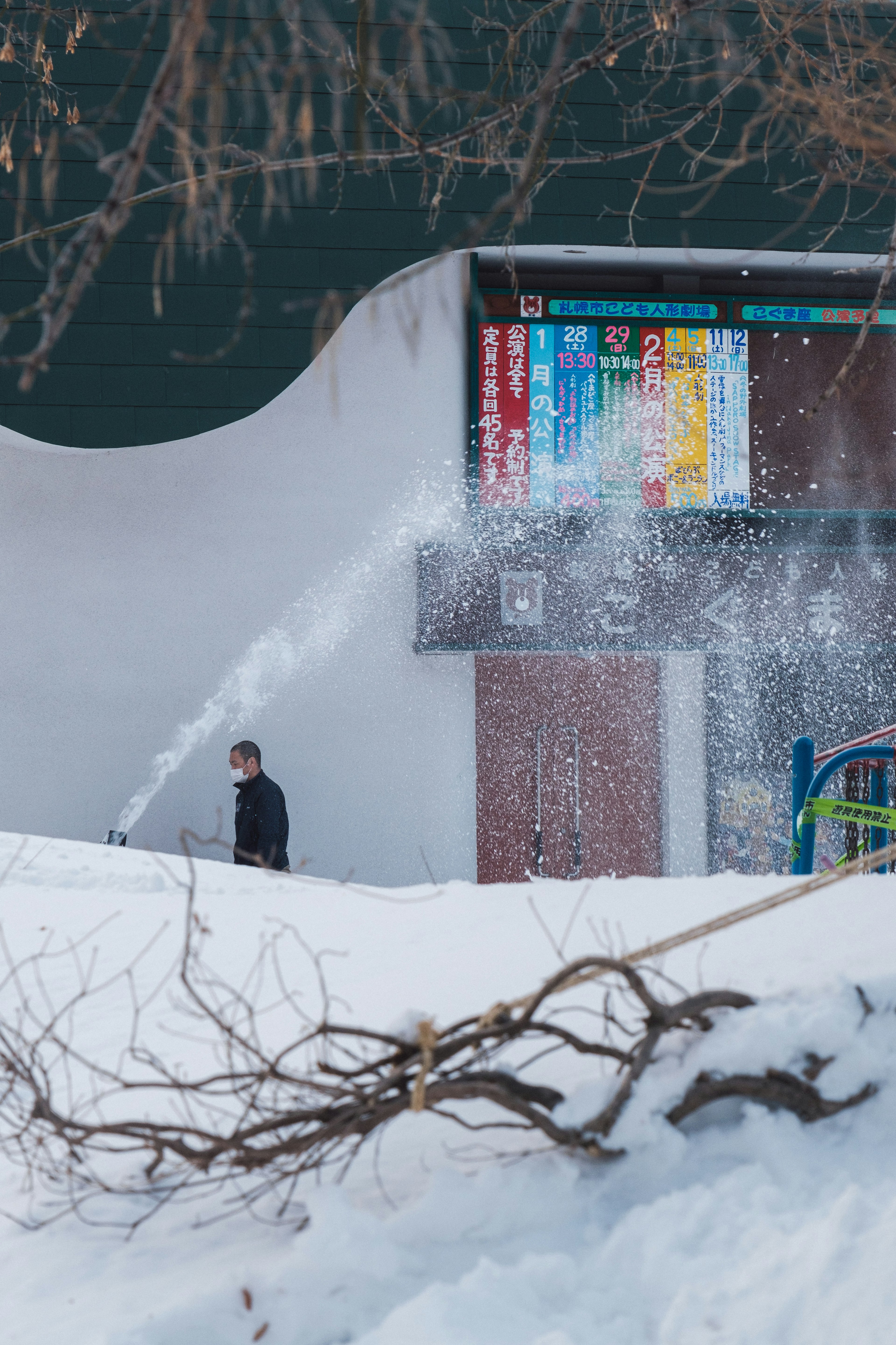 雪の中で作業する人物と色とりどりの看板がある建物