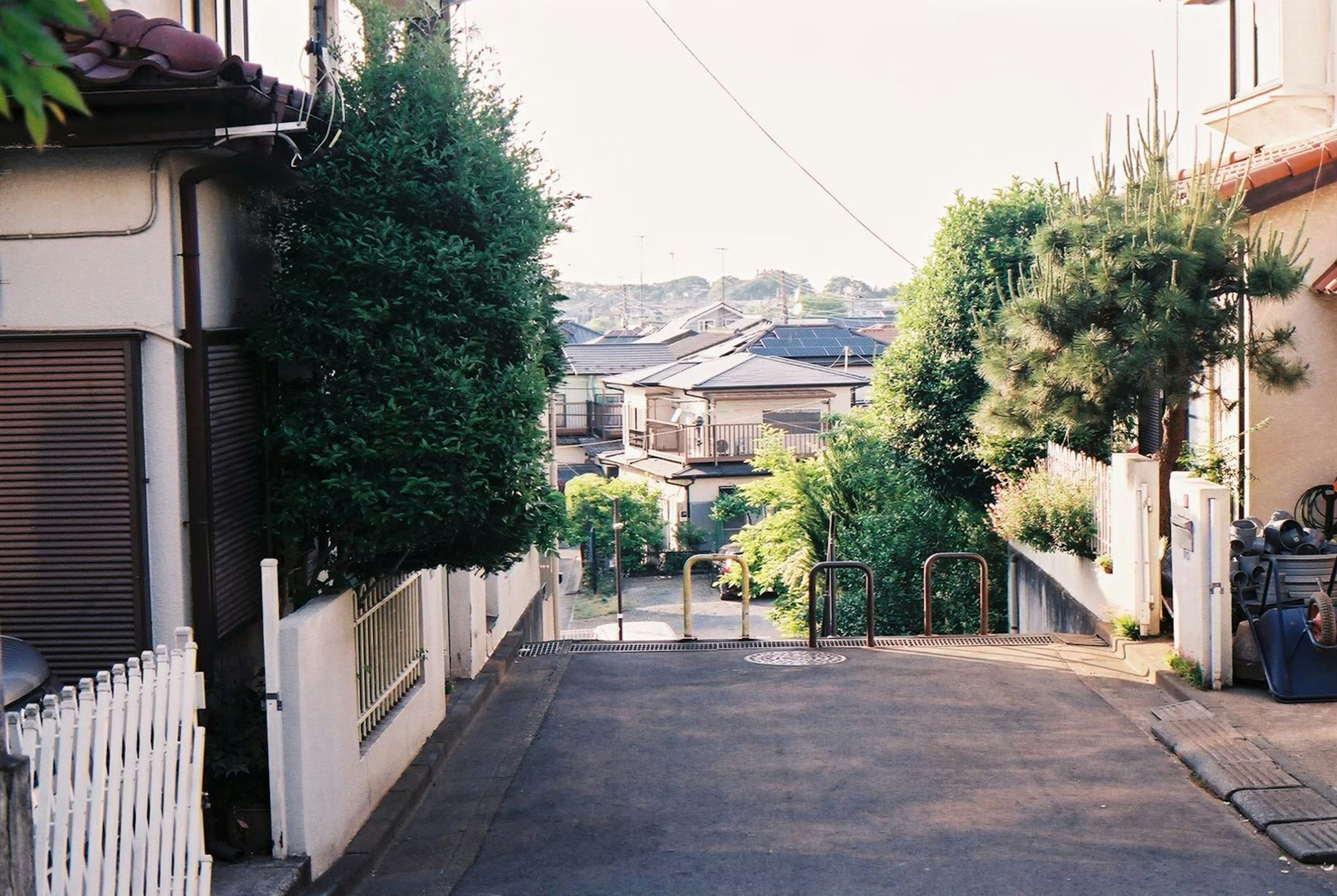 静かな住宅街の坂道が続き、緑の木々と家々が見える