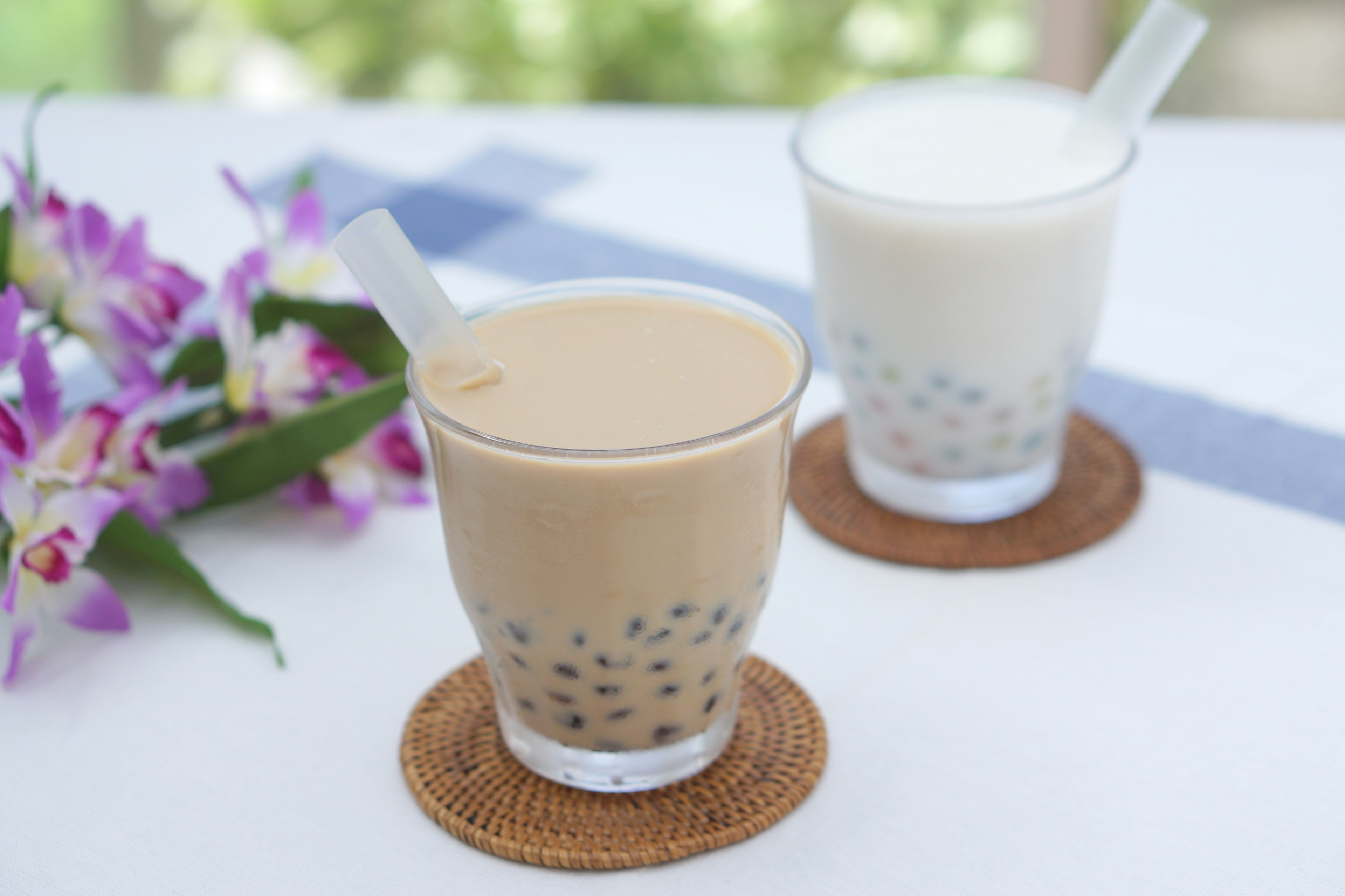 Brown bubble tea and white milk beverage placed on a table with a floral backdrop