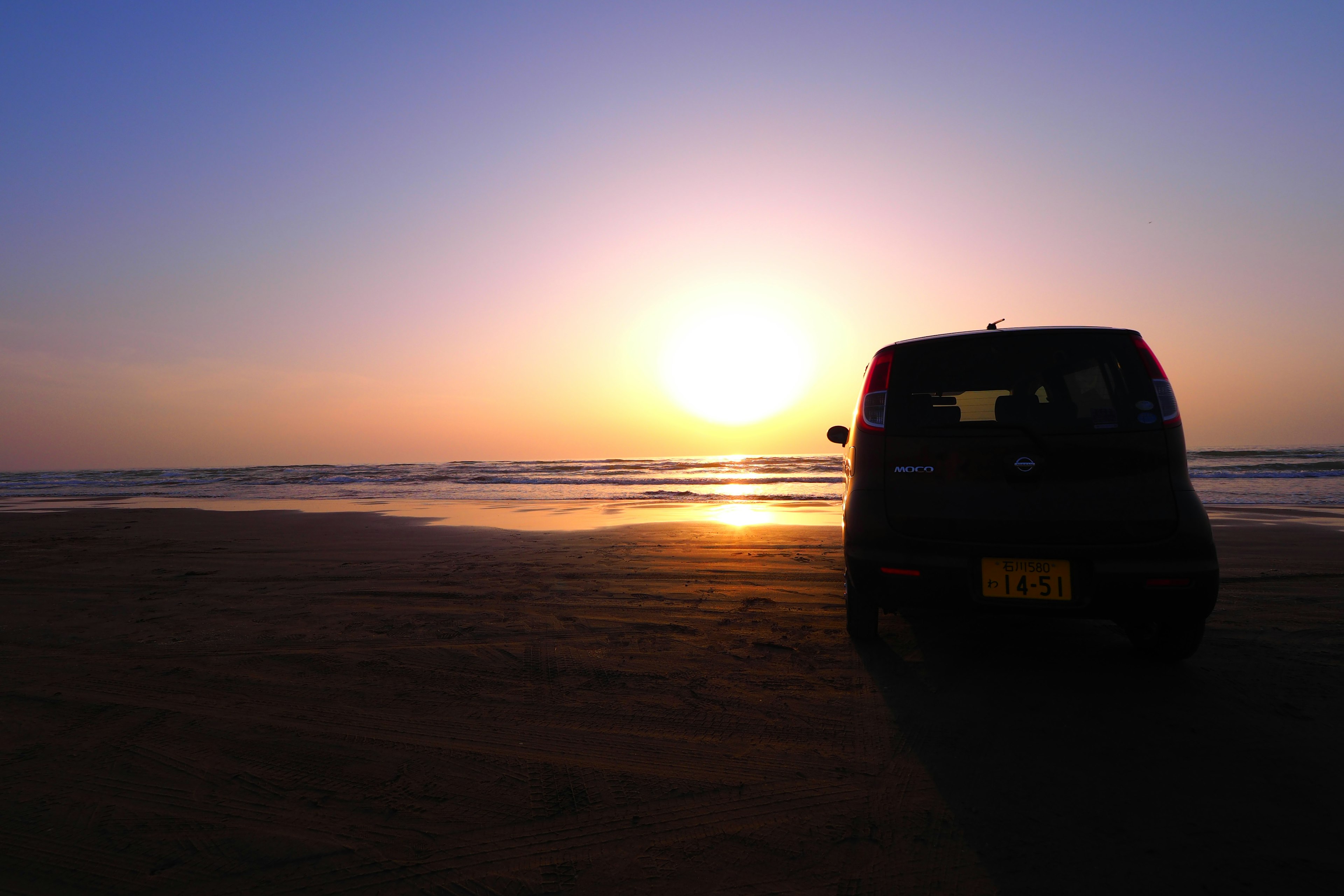 Mobil hitam diparkir di pantai dengan matahari terbenam