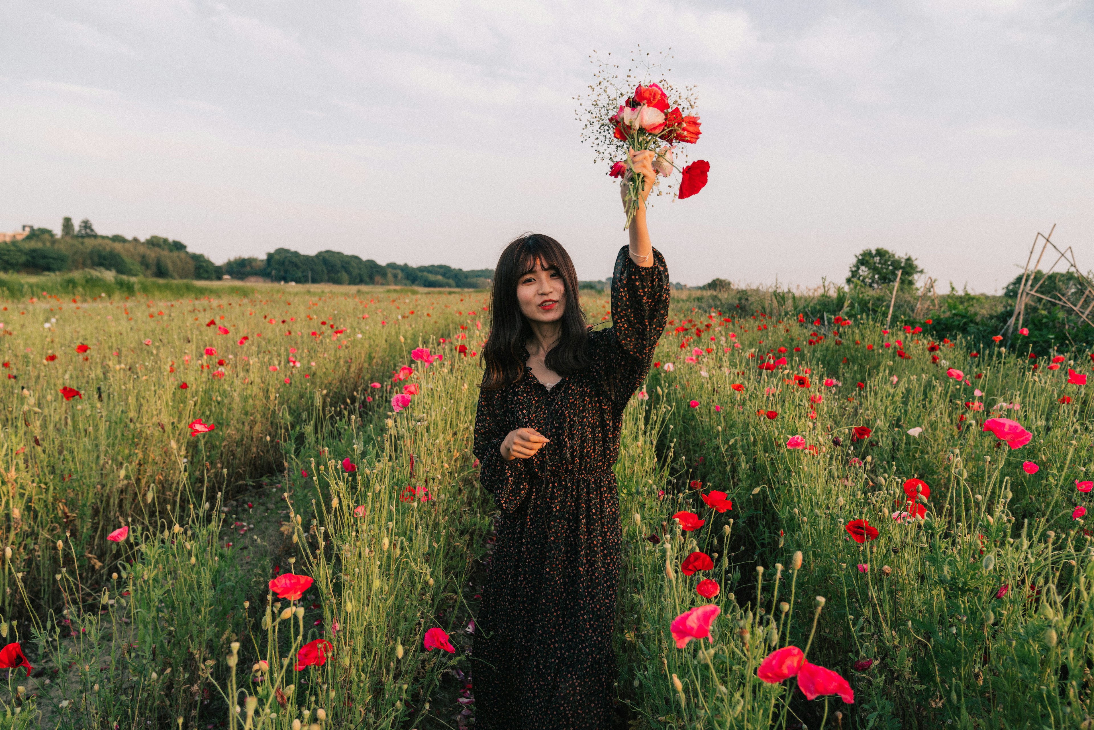 赤い花に囲まれた女性が花束を持っている風景