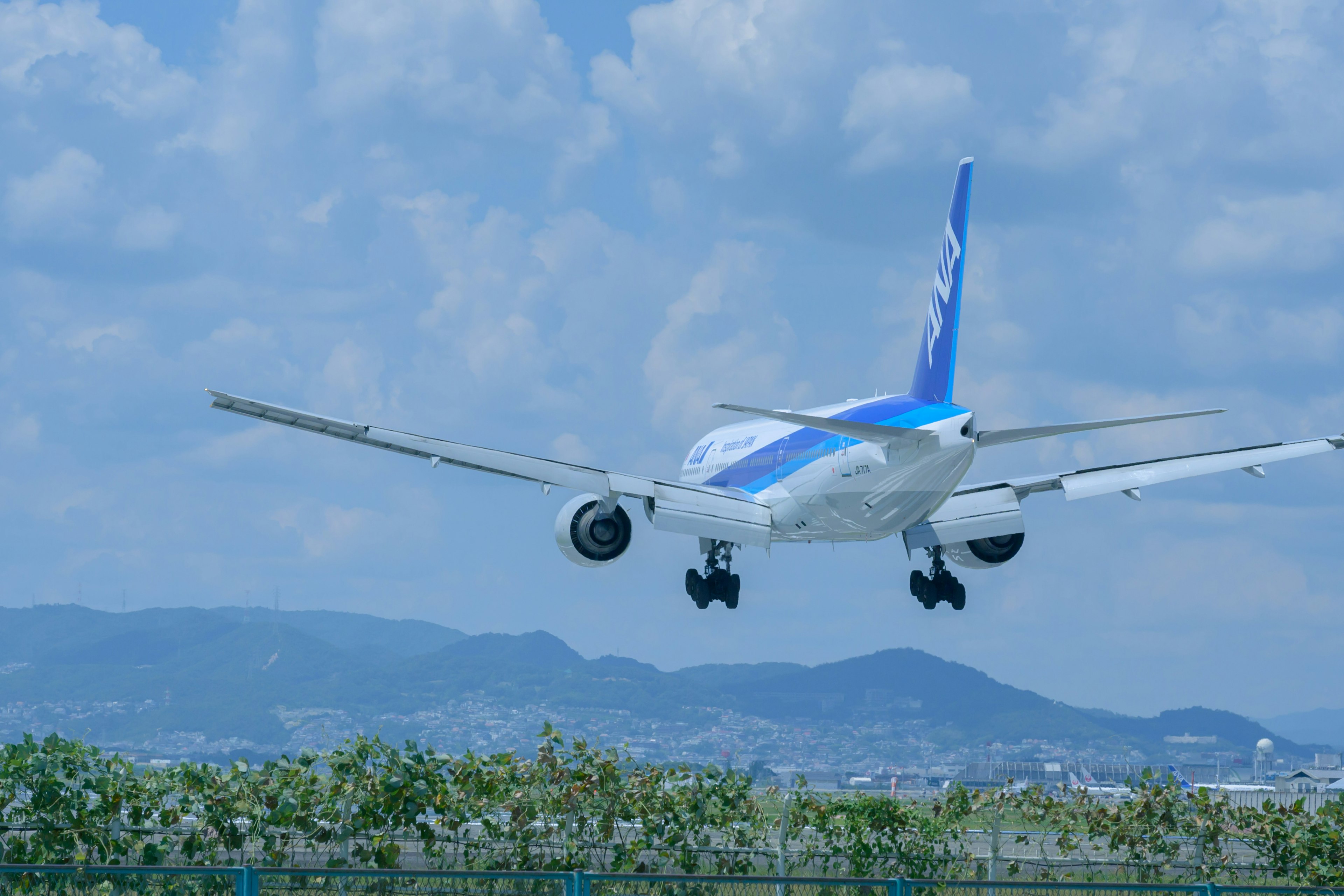 Vista di un aereo in atterraggio contro un cielo blu con montagne sullo sfondo