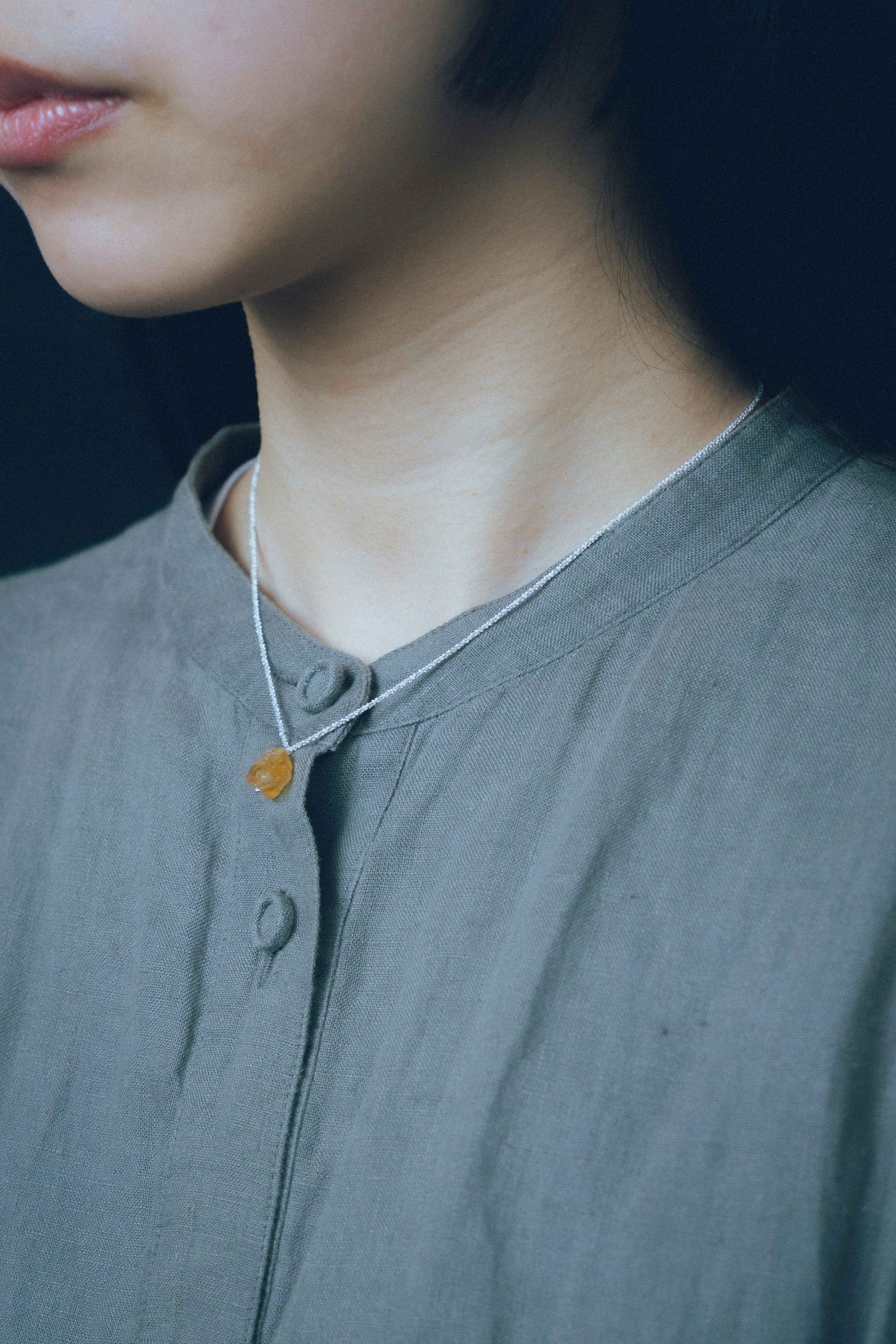 Close-up of a woman wearing a simple necklace and a gray blouse