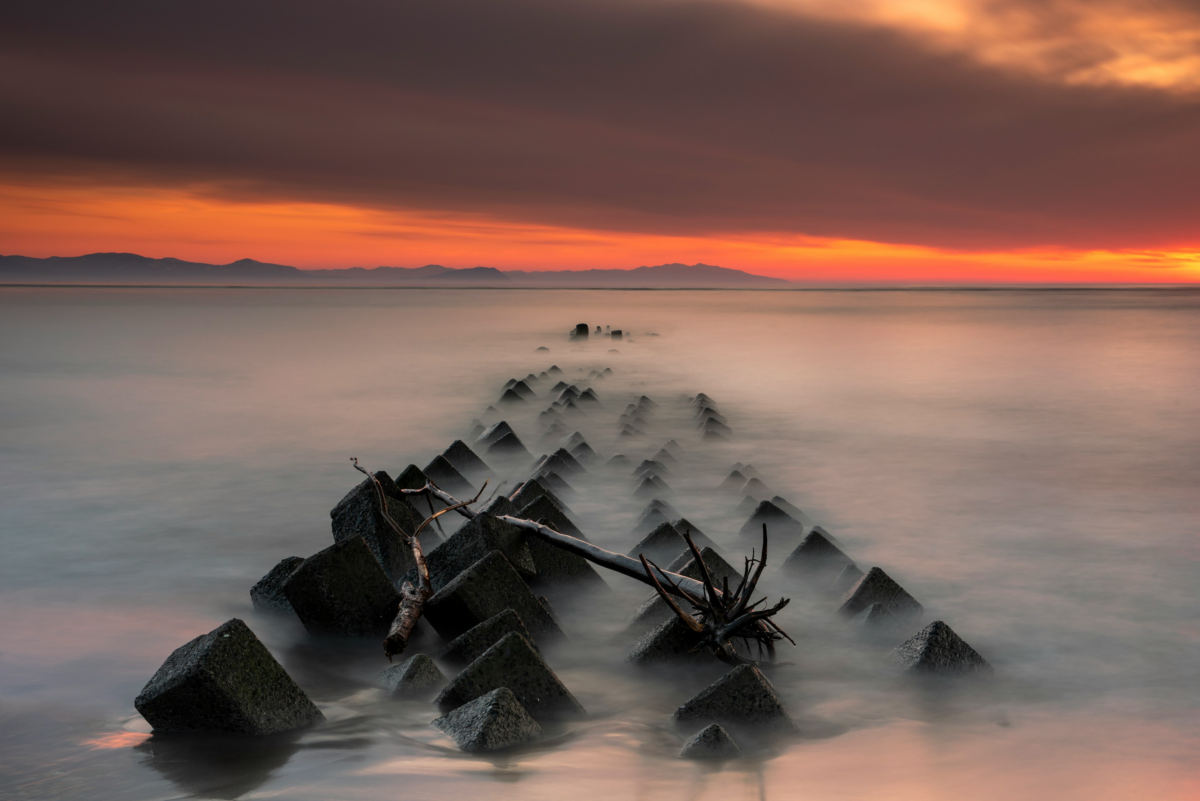 Jetée rocheuse le long d'une plage calme avec un ciel de coucher de soleil vibrant