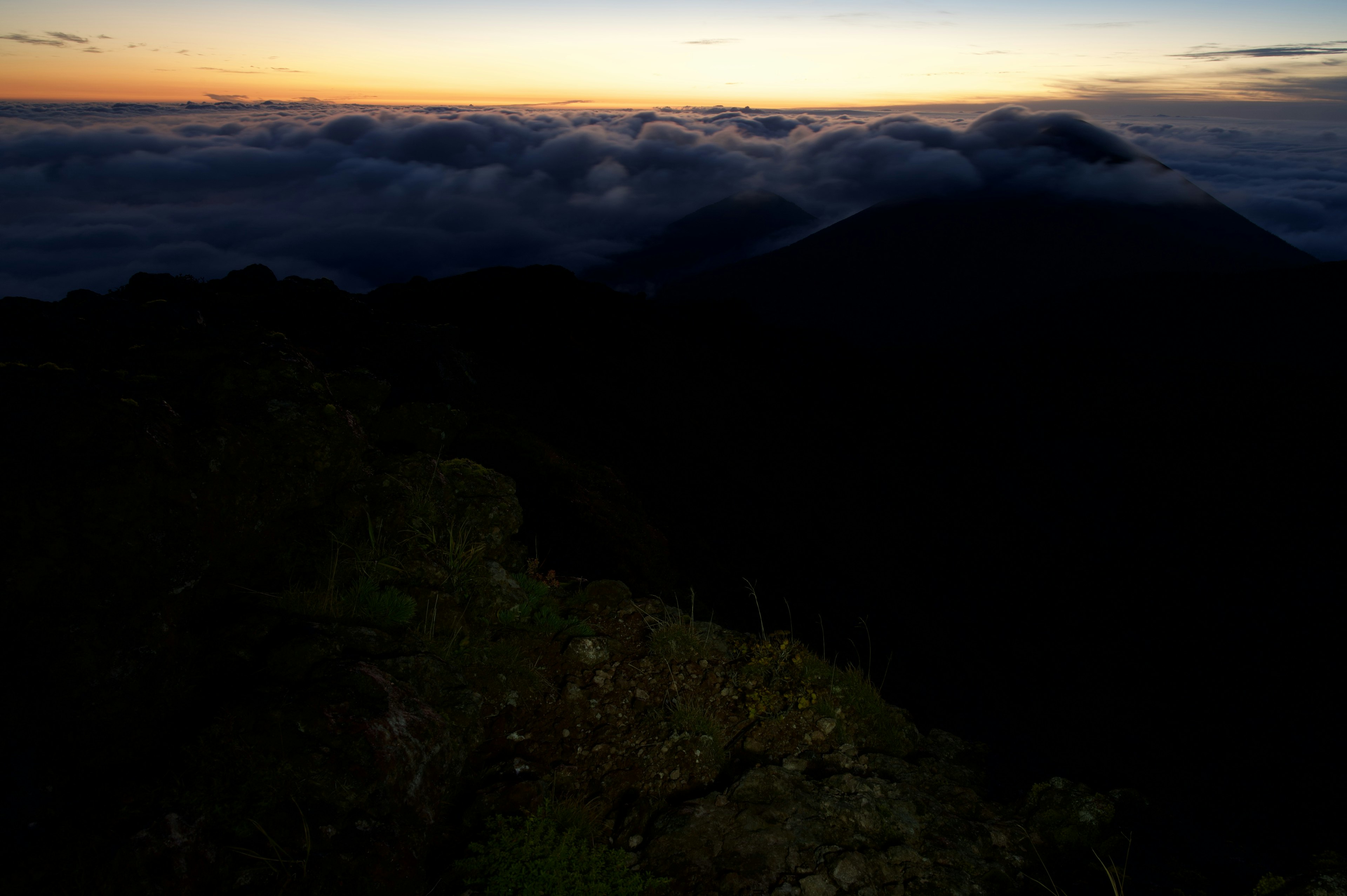 Matahari terbenam di atas awan dengan siluet gunung dan medan gelap