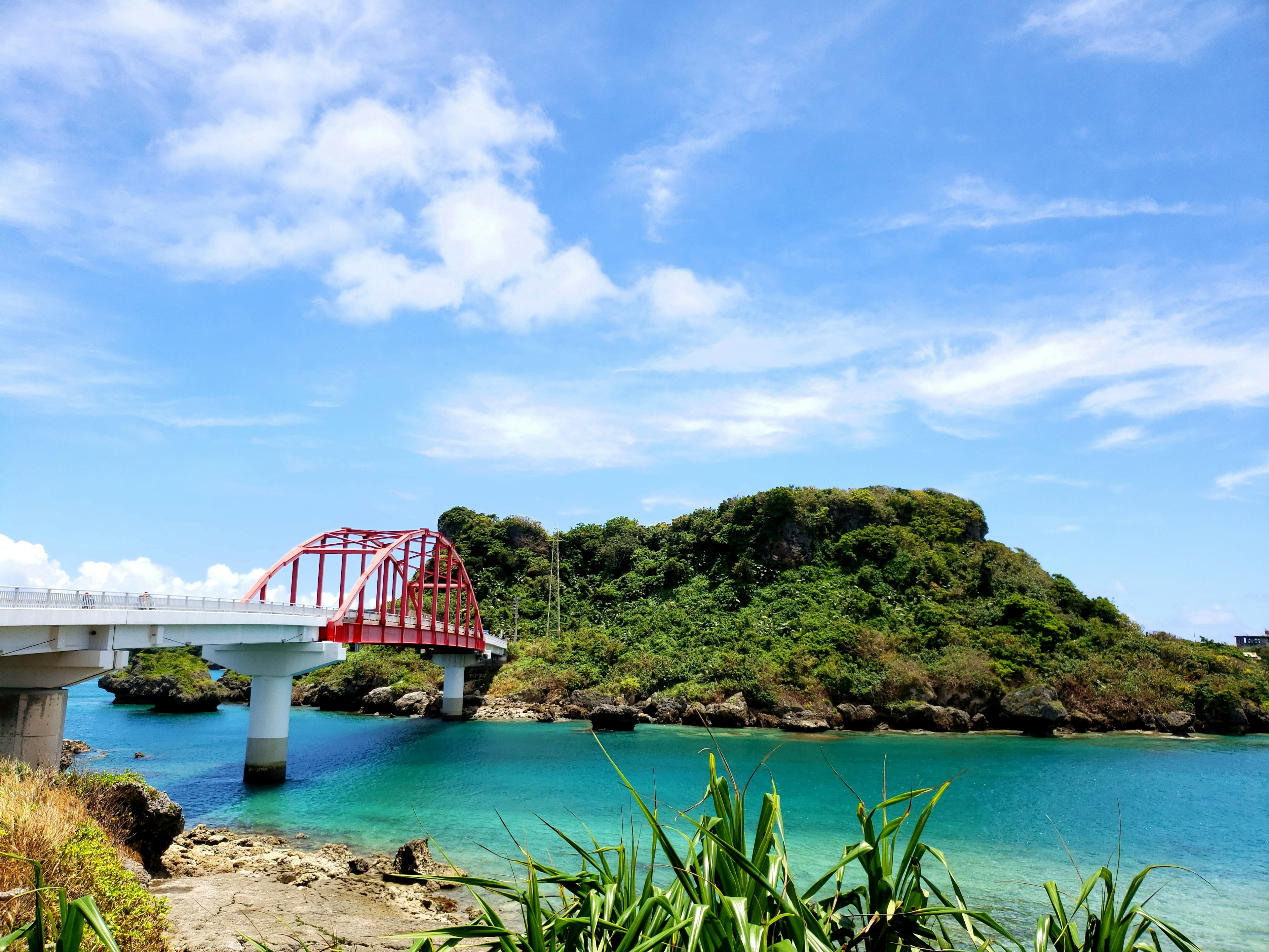 Vista de un puente rojo sobre agua turquesa con una isla verde