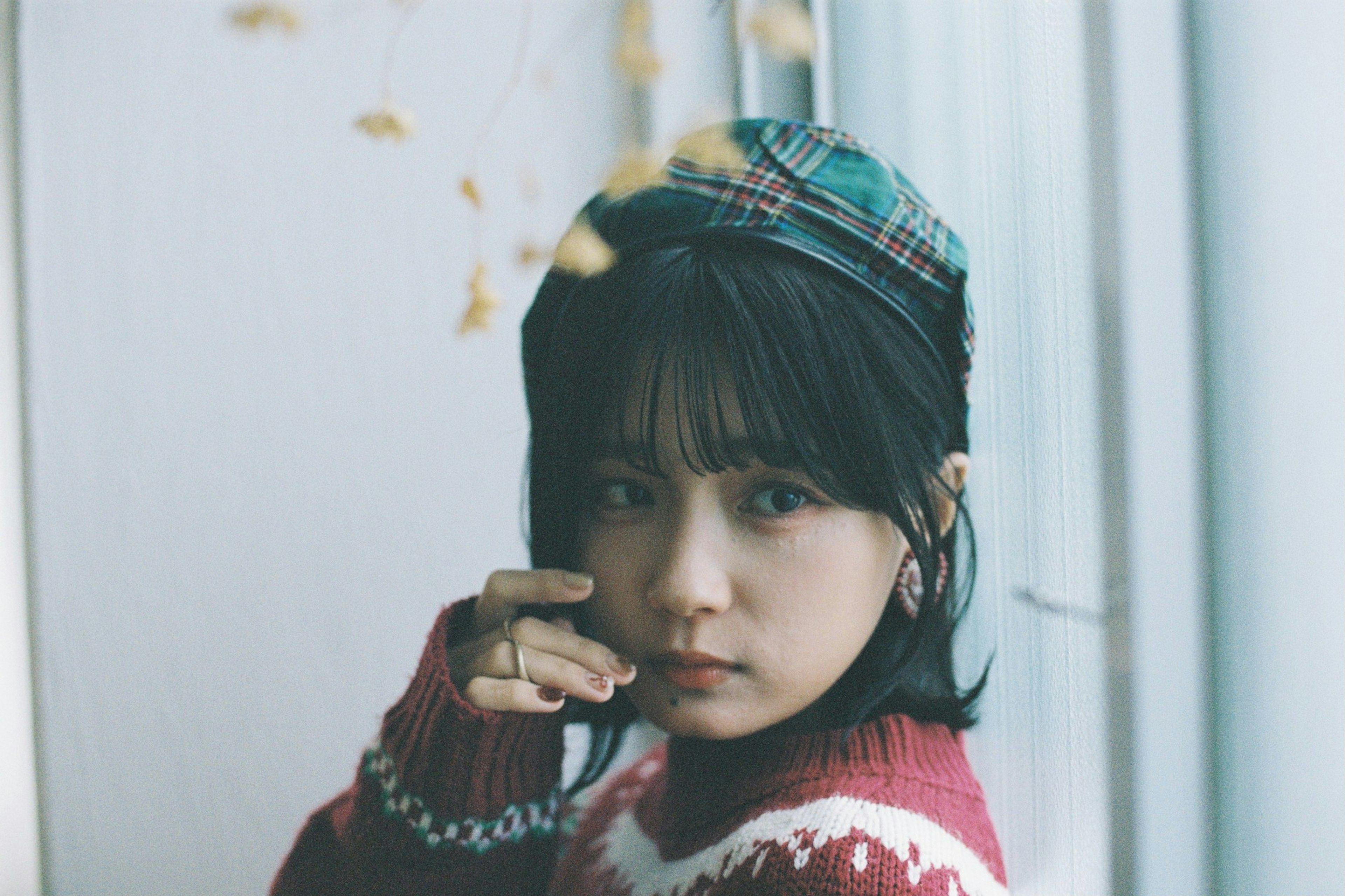 Portrait of a woman near a window wearing a checkered hat and a red and white sweater, soft light illuminating her face