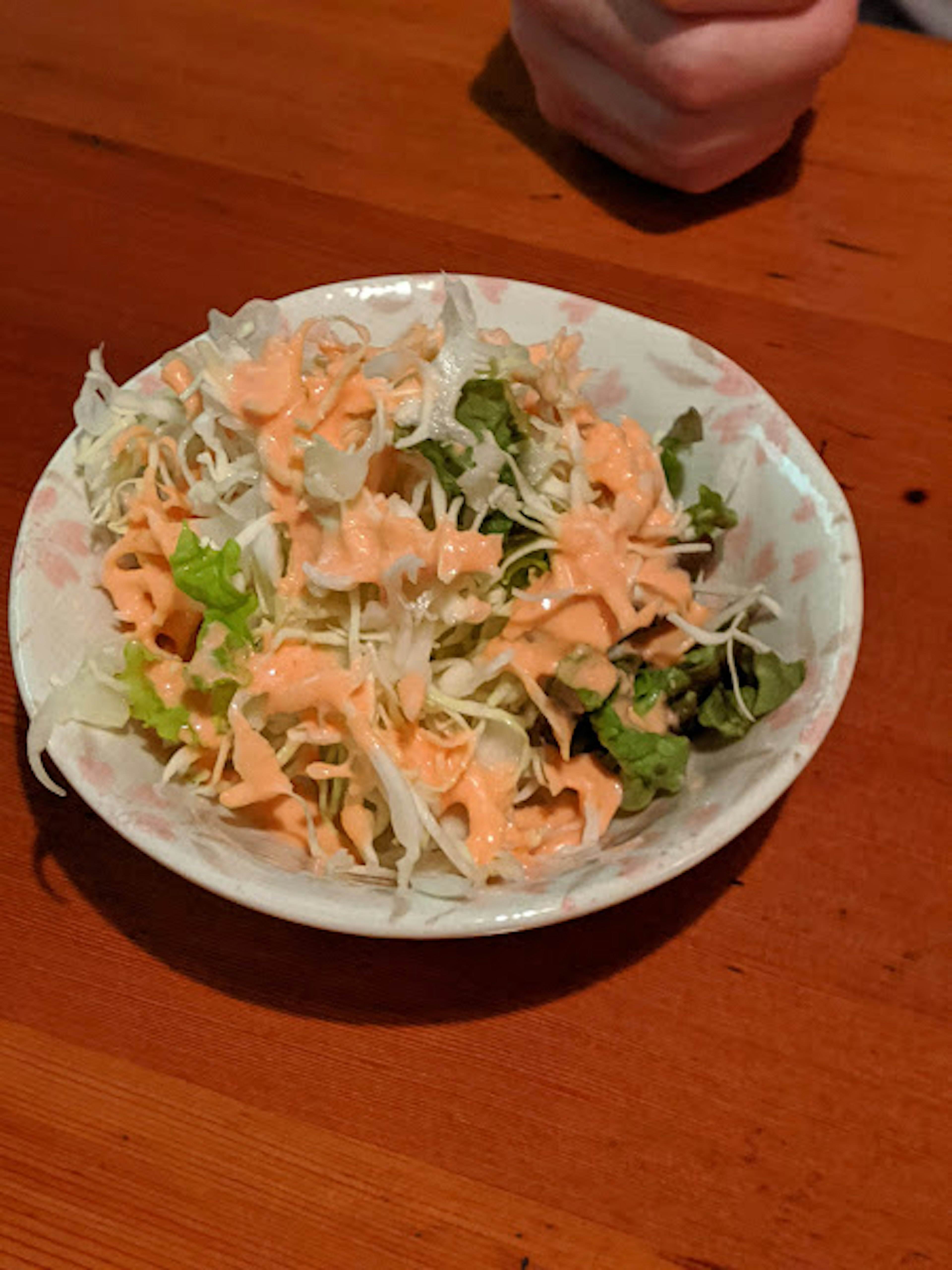 Salad served in a white bowl featuring fresh cabbage and lettuce topped with pink dressing