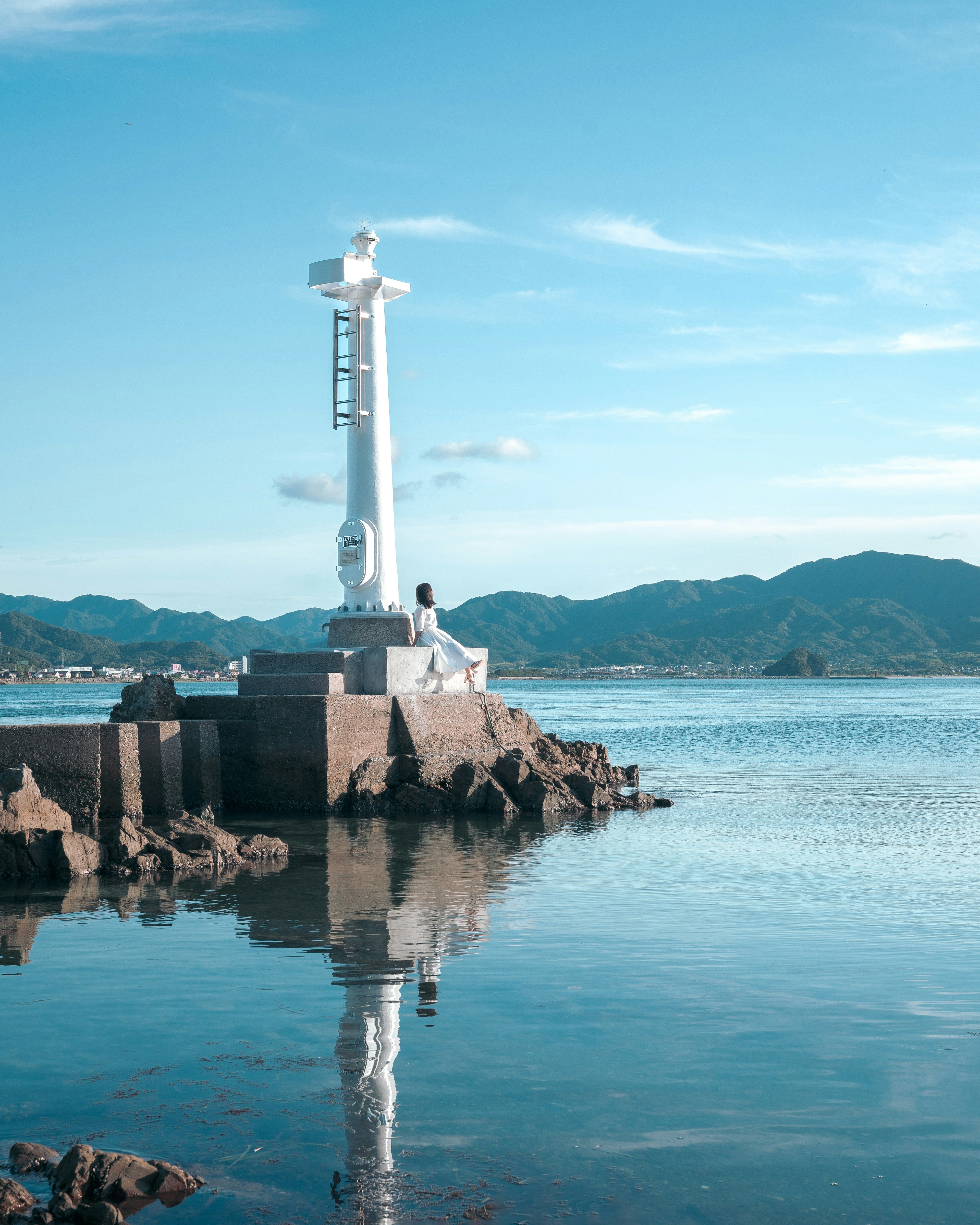 White lighthouse under blue sky with calm water reflection