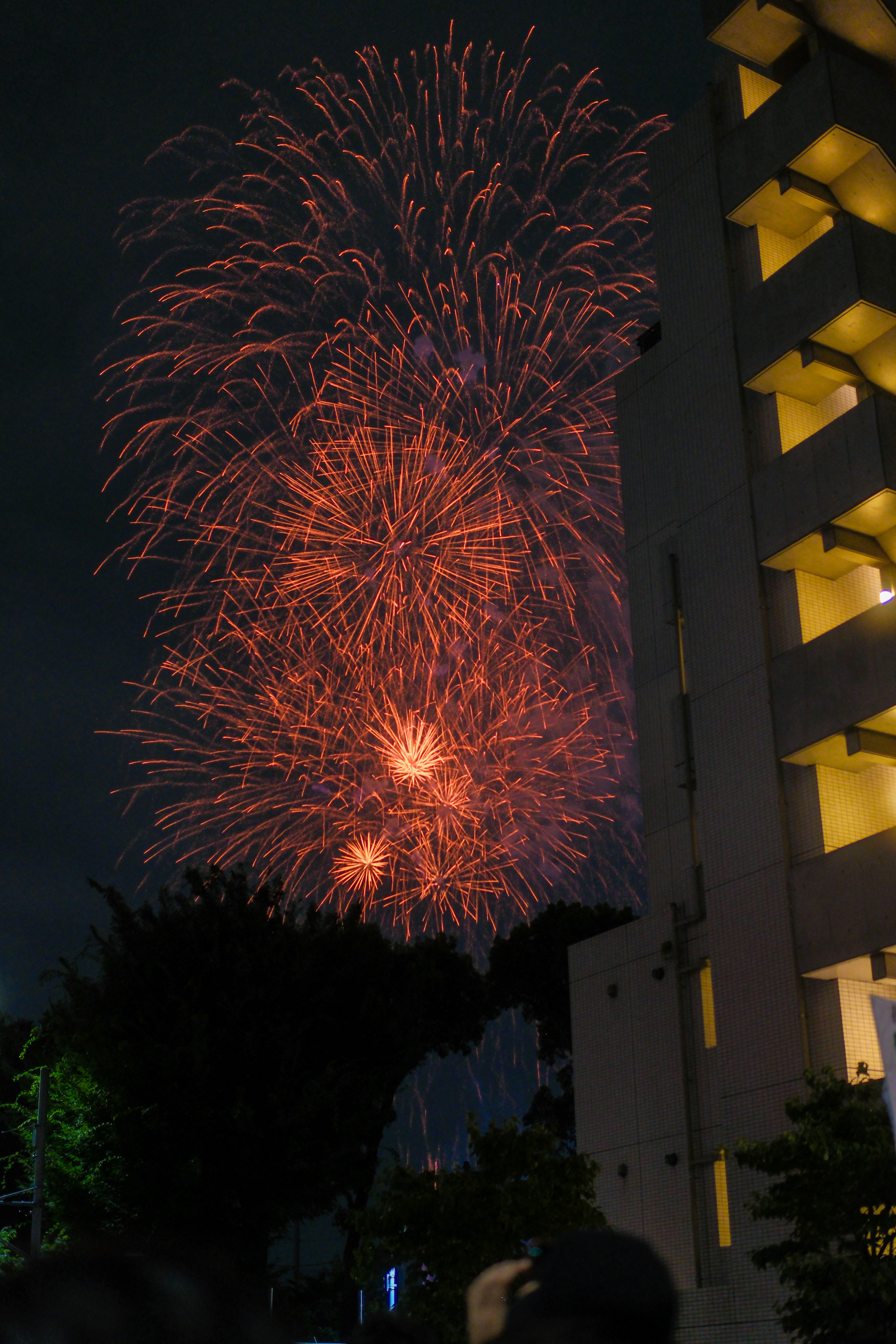 Fuochi d'artificio arancioni che esplodono nel cielo notturno con silhouette di edificio