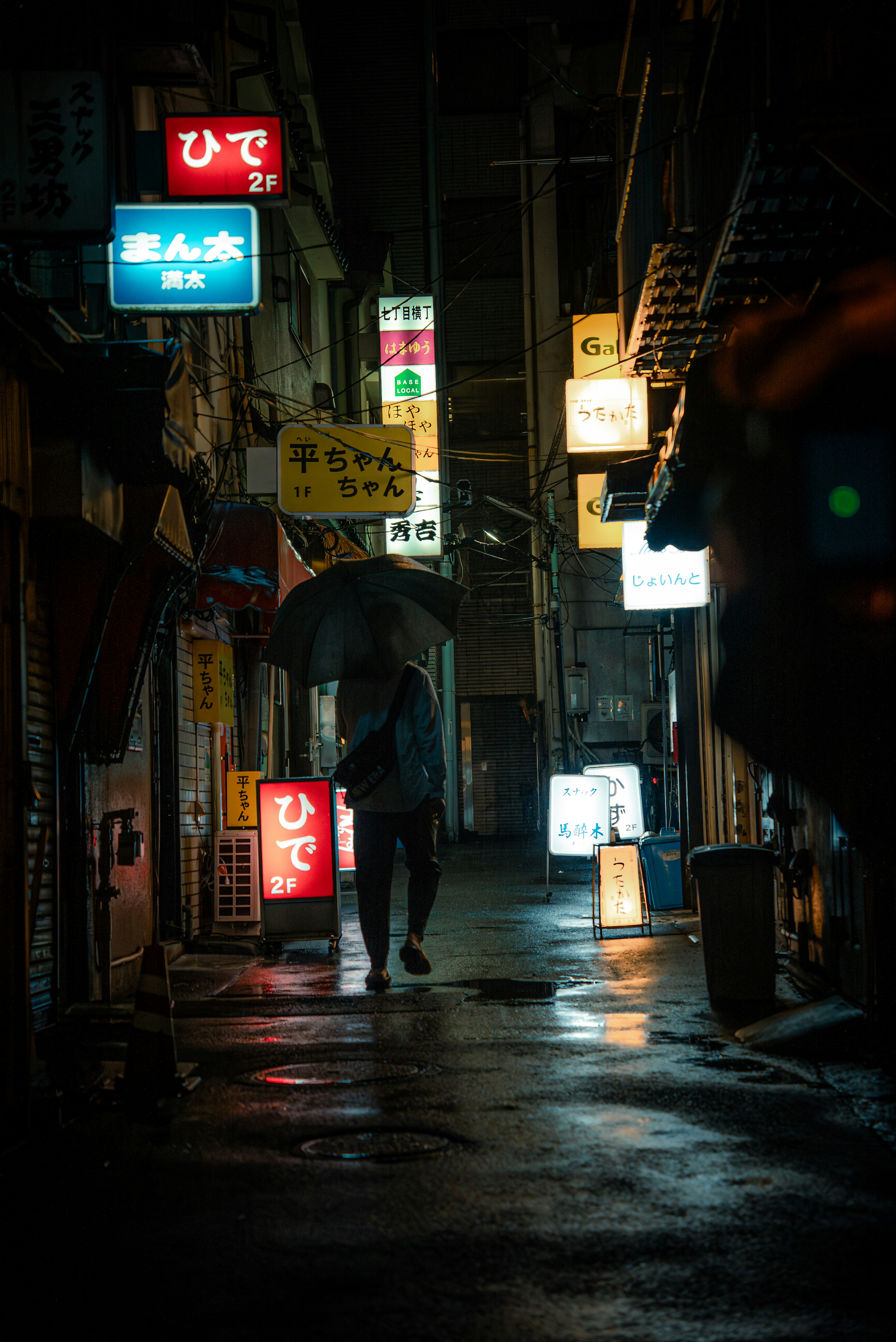 雨の中で傘を持った人が暗い路地を歩いている街の風景