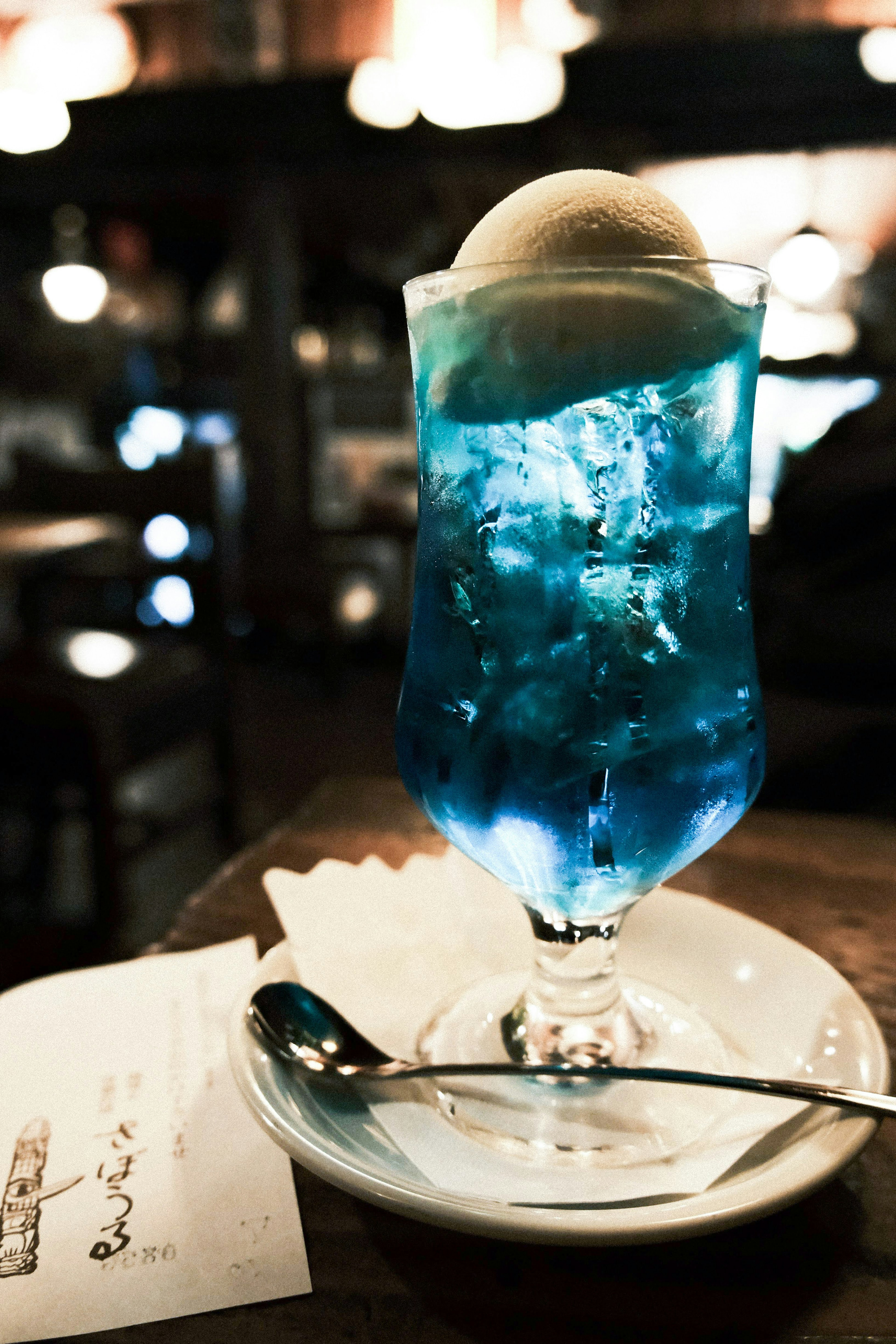 A glass of blue drink topped with ice cream served on a plate