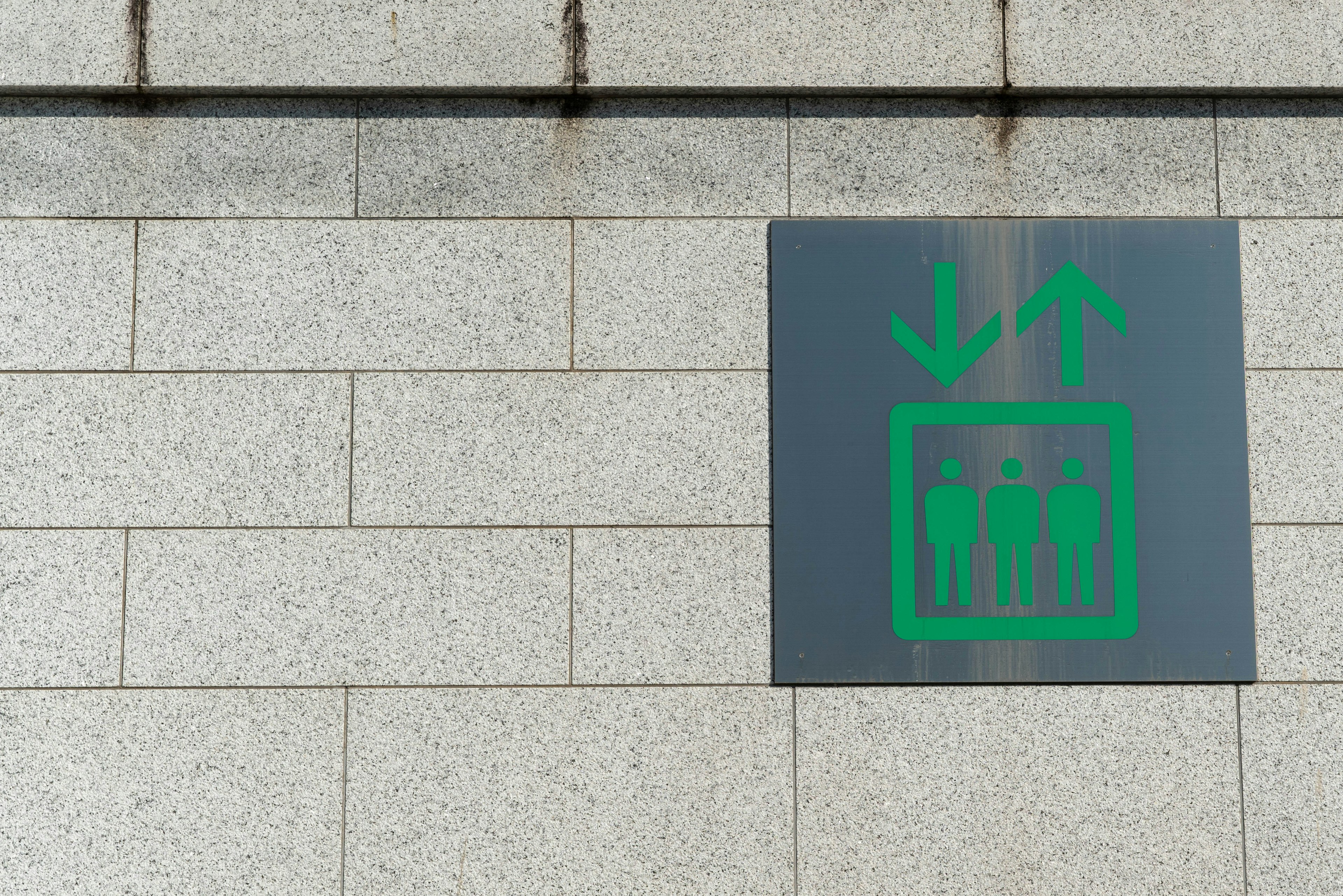 A gray wall-mounted sign featuring an elevator icon with upward and downward arrows