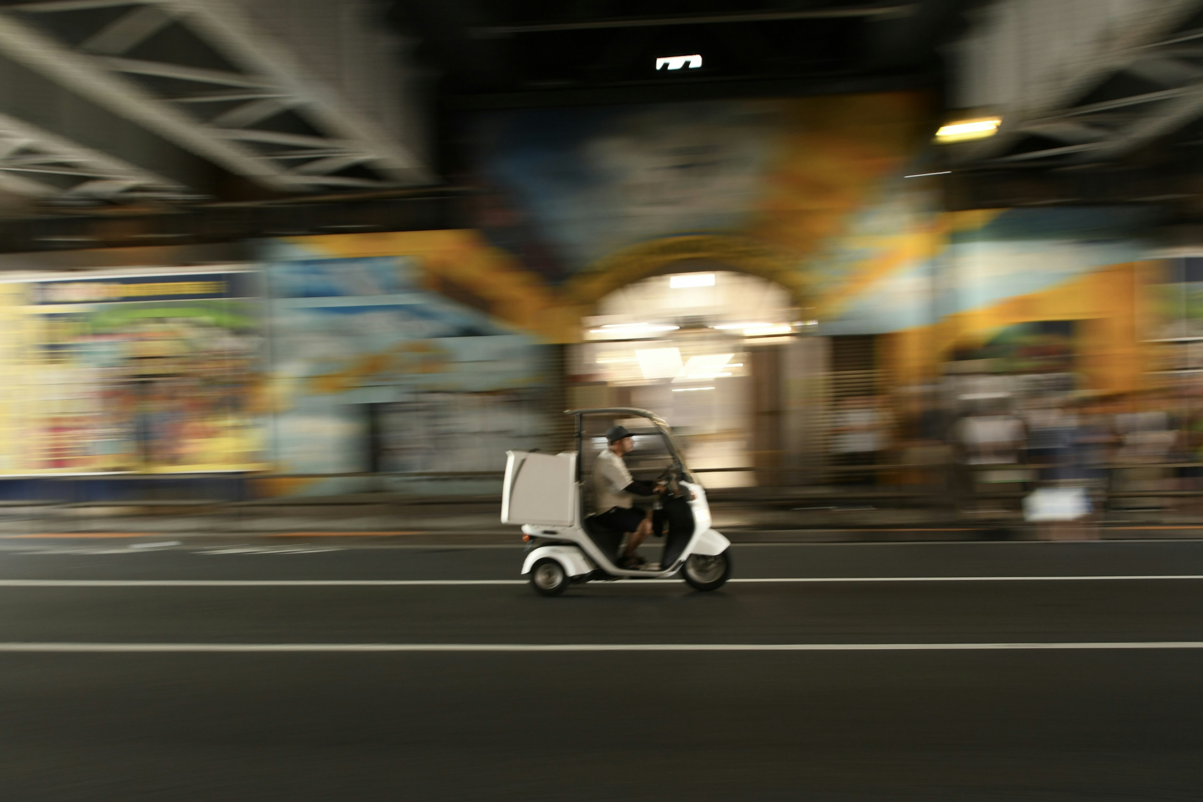 A white tricycle in motion with colorful murals in the background