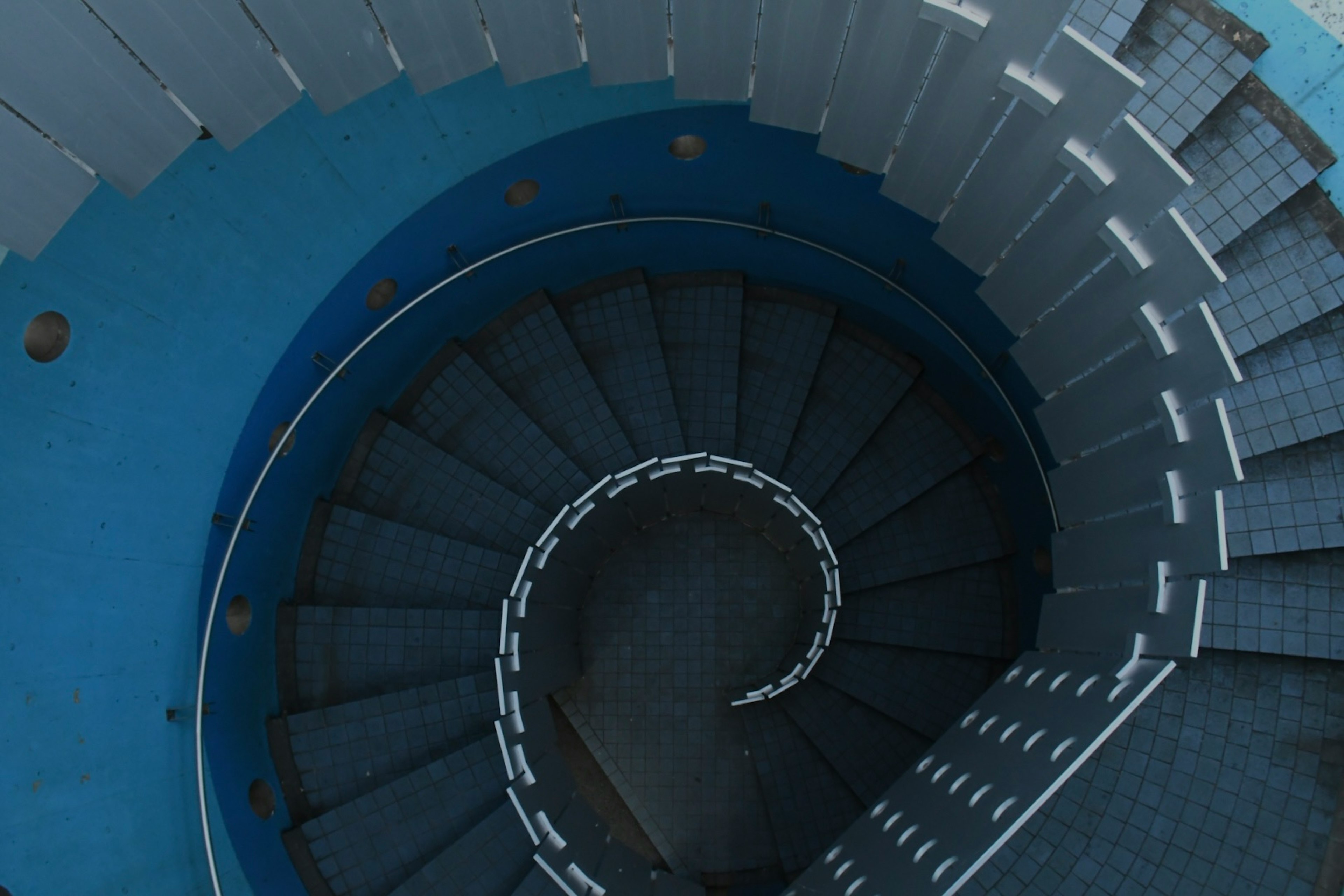 View from above of a blue spiral staircase featuring white railings