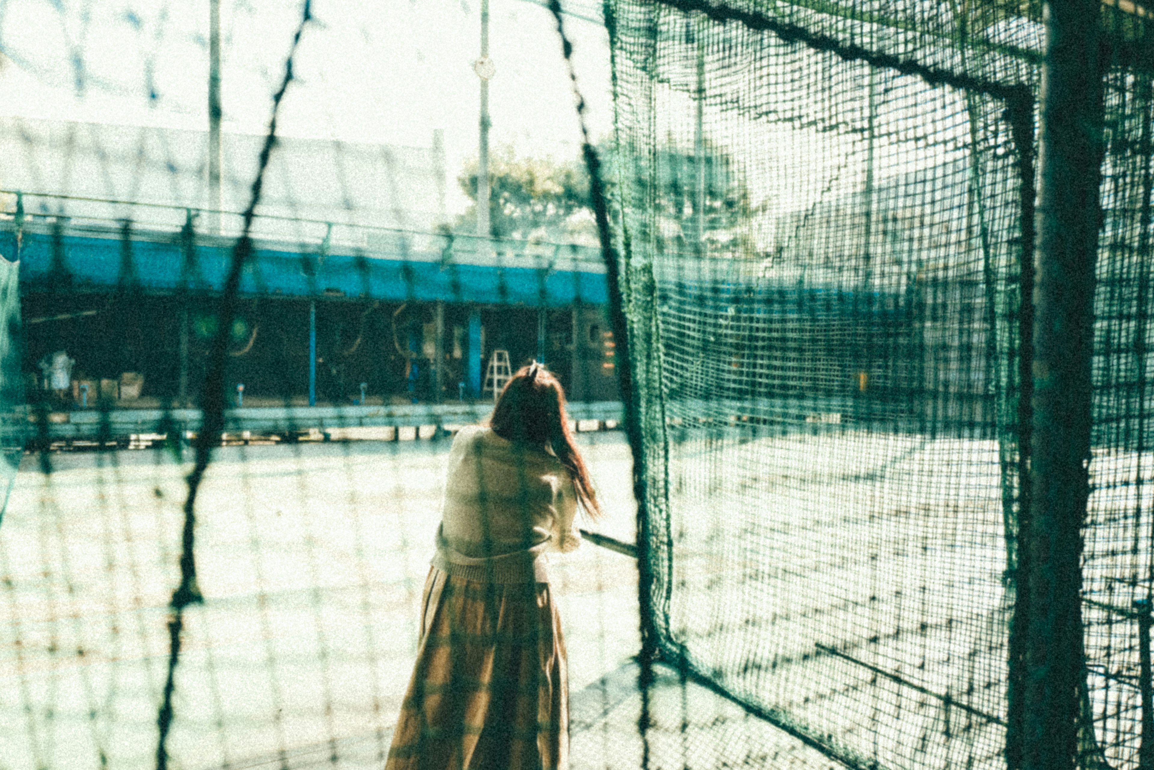 Woman looking back through a net with a tennis court in the background