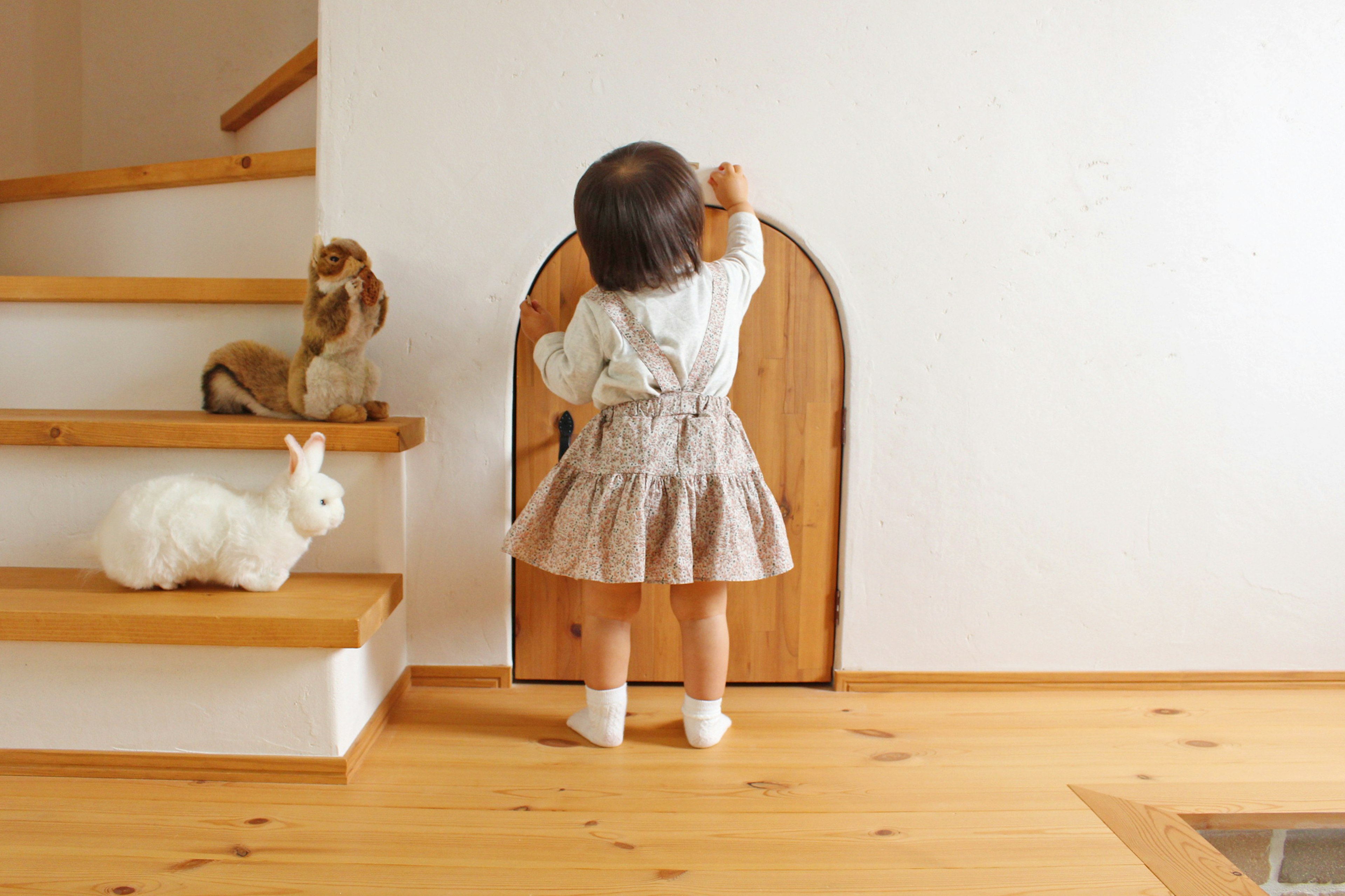 Una niña pequeña tocando una puerta de madera con un conejo y un perro cerca de las escaleras