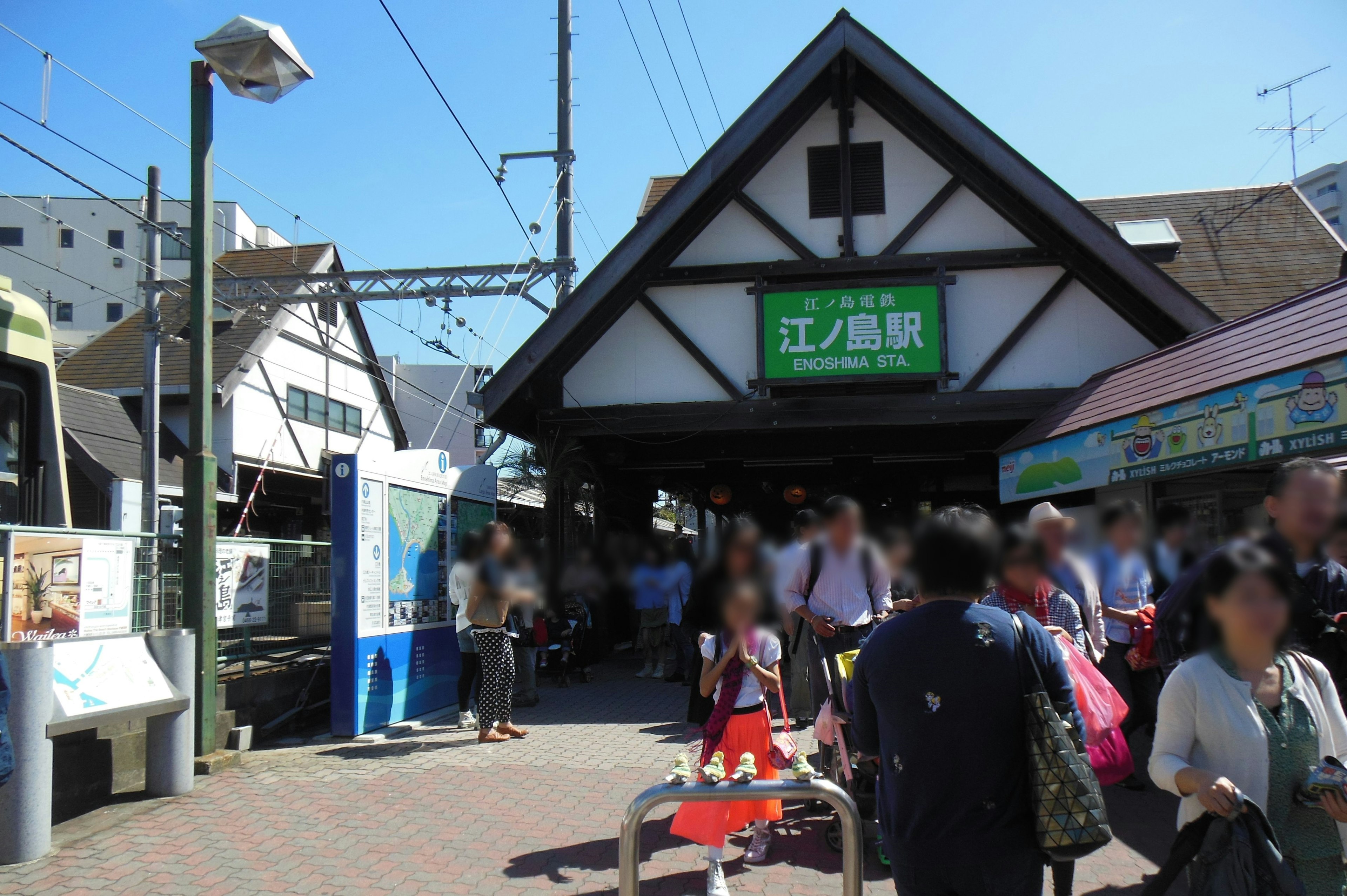 Entrada de estación de tren concurrida con gente y paisaje circundante